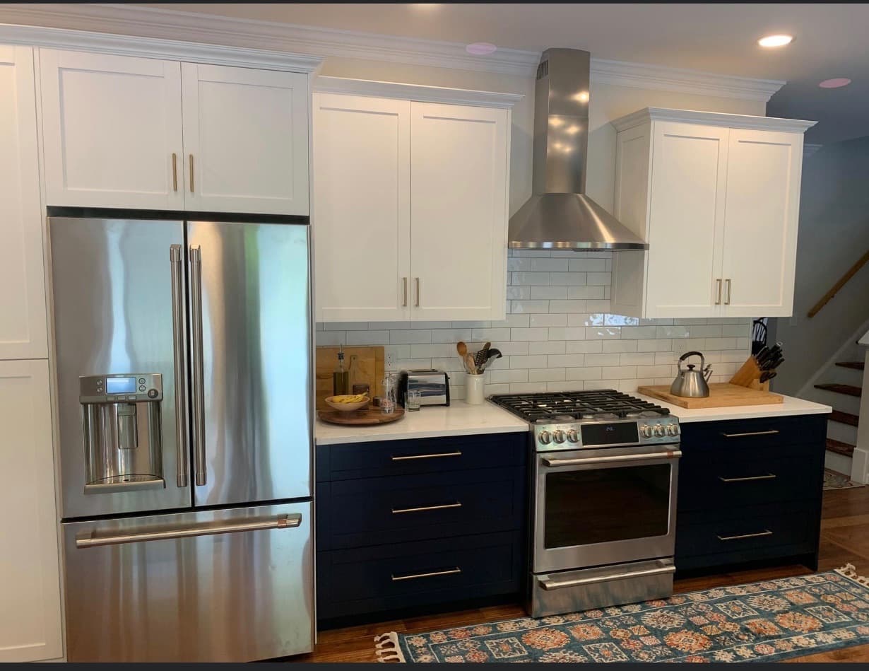 A transitional kitchen with white upper cabinets, navy blue base cabinets, and white subway tile backsplash