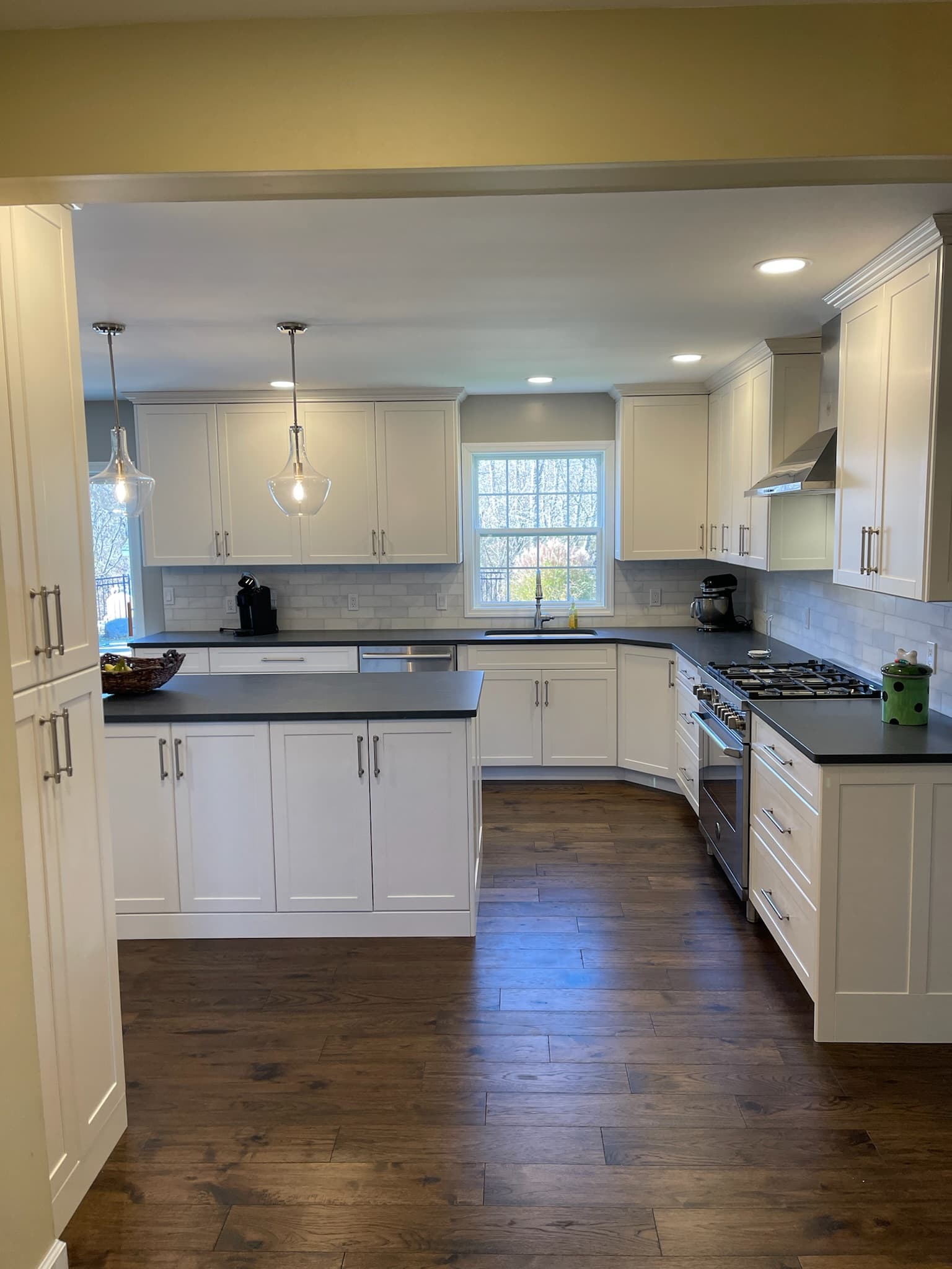 Wide view of a transitional kitchen featuring white shaker cabinets, dark countertops, and a central island