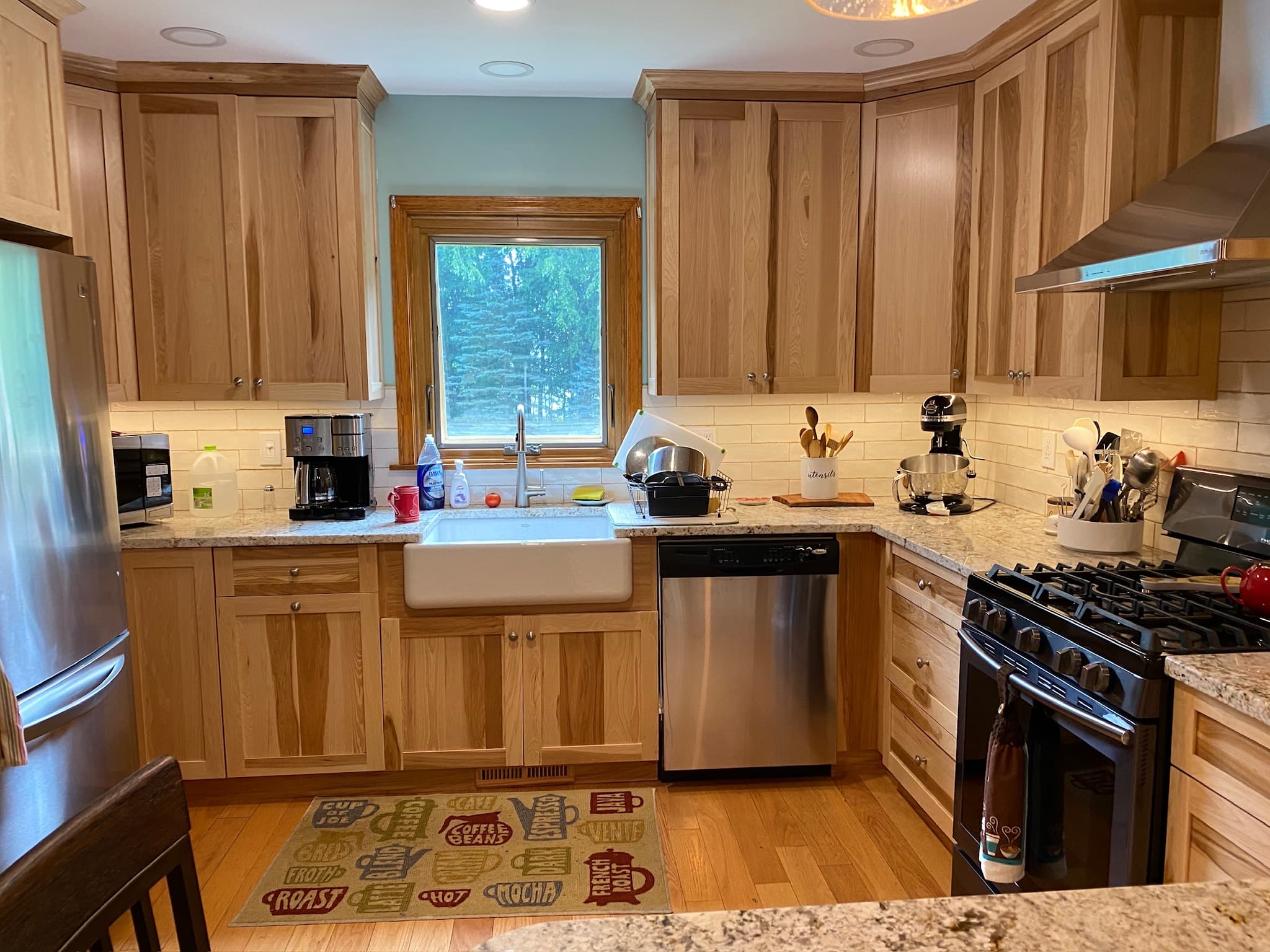 Transitional kitchen with natural wood cabinets, granite countertops, a farmhouse sink, and stainless steel appliances