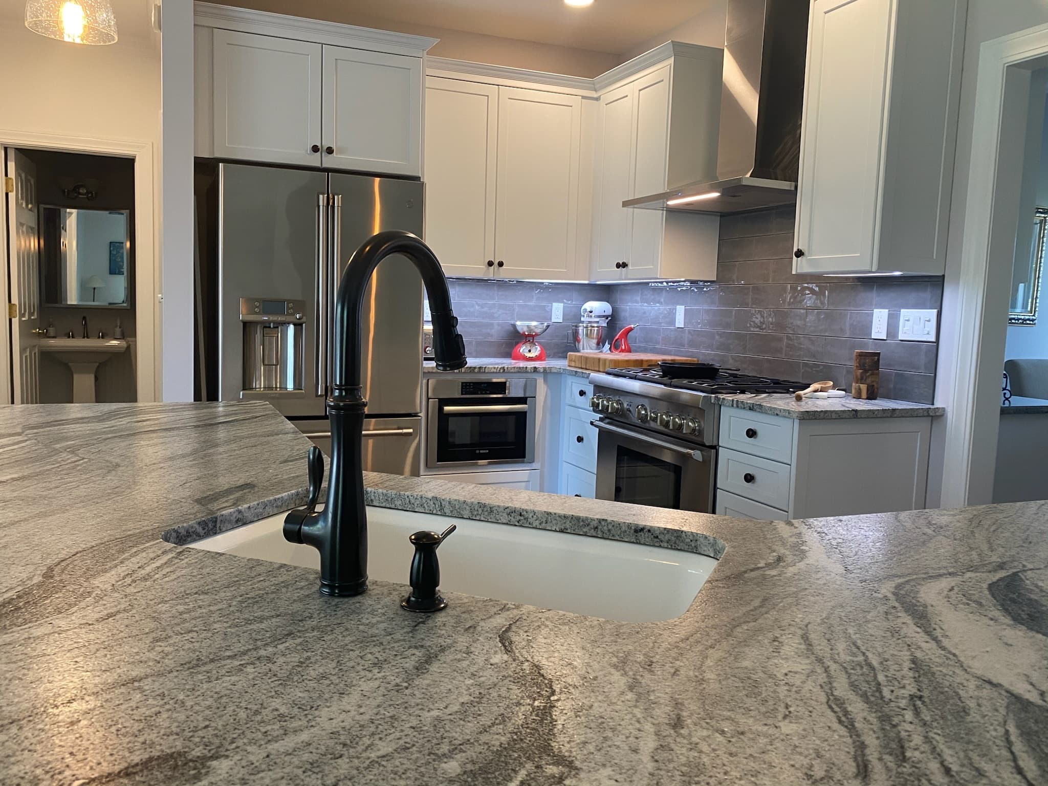 Wide view of a transitional kitchen with white shaker cabinets, granite countertops, and matte black fixtures