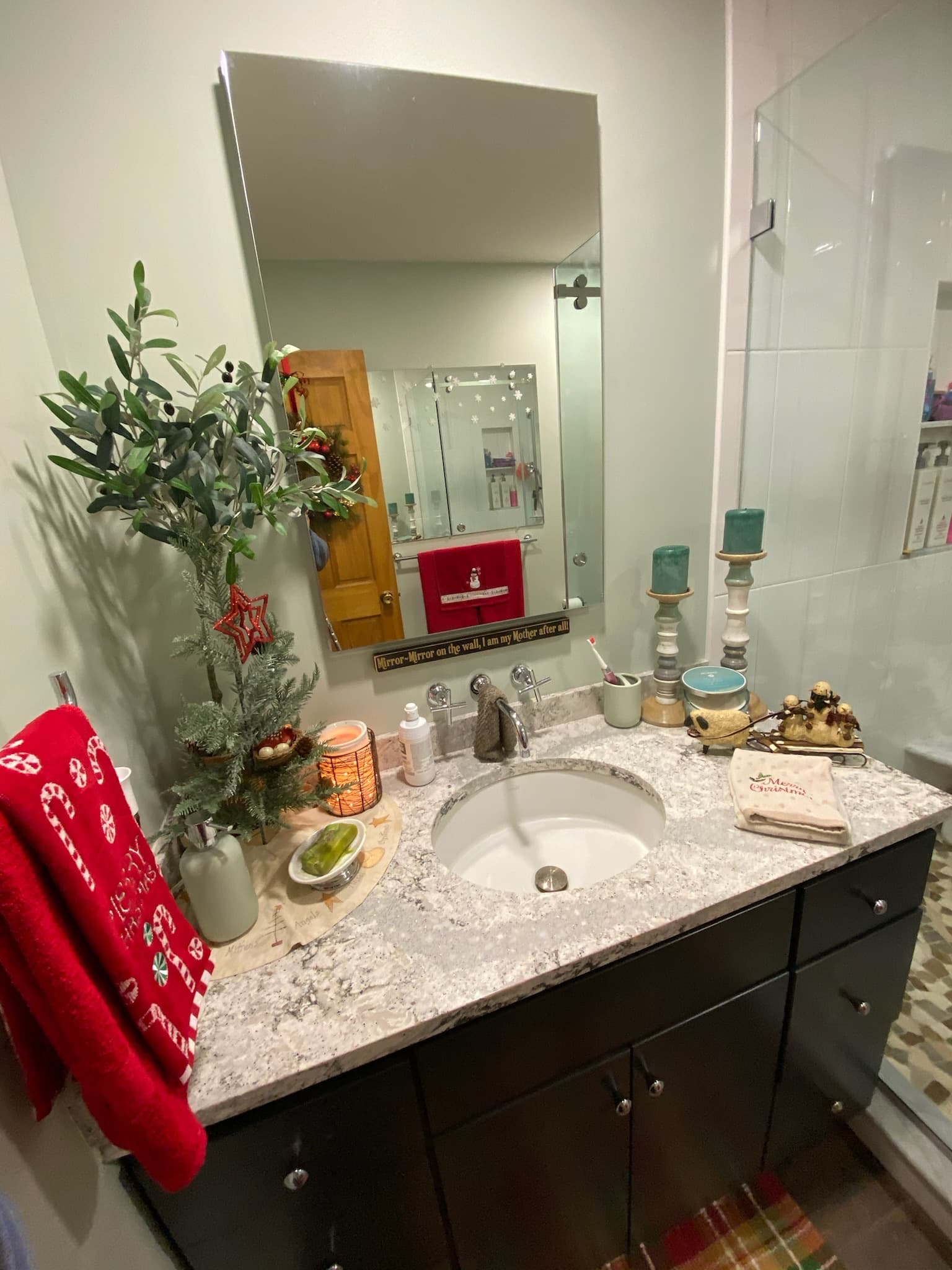 A black single vanity with a granite countertop and an undermount sink, reflecting a mirror with Christmas decorations