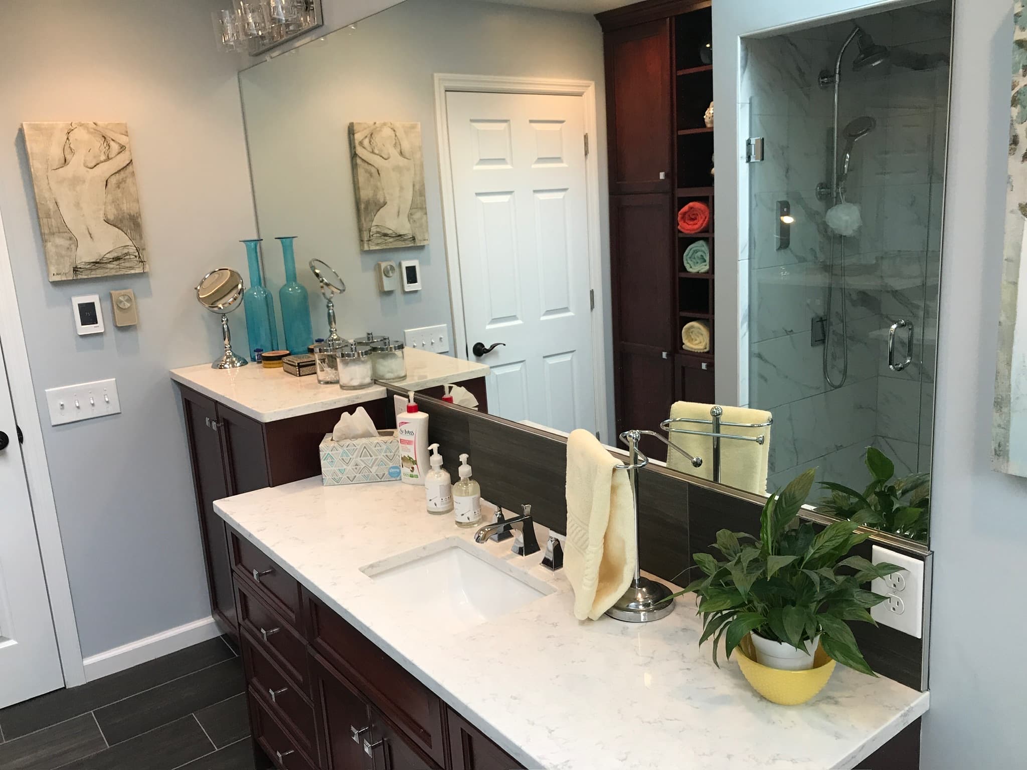 A transitional bathroom with dark wood double vanity cabinets, white engineered quartz countertops, and a glass-enclosed walk-in shower