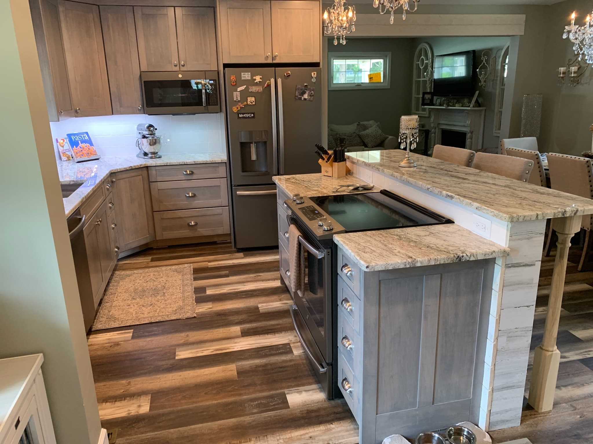 A transitional kitchen features gray cabinets, granite countertops, an island with cooktop, and an extended breakfast bar