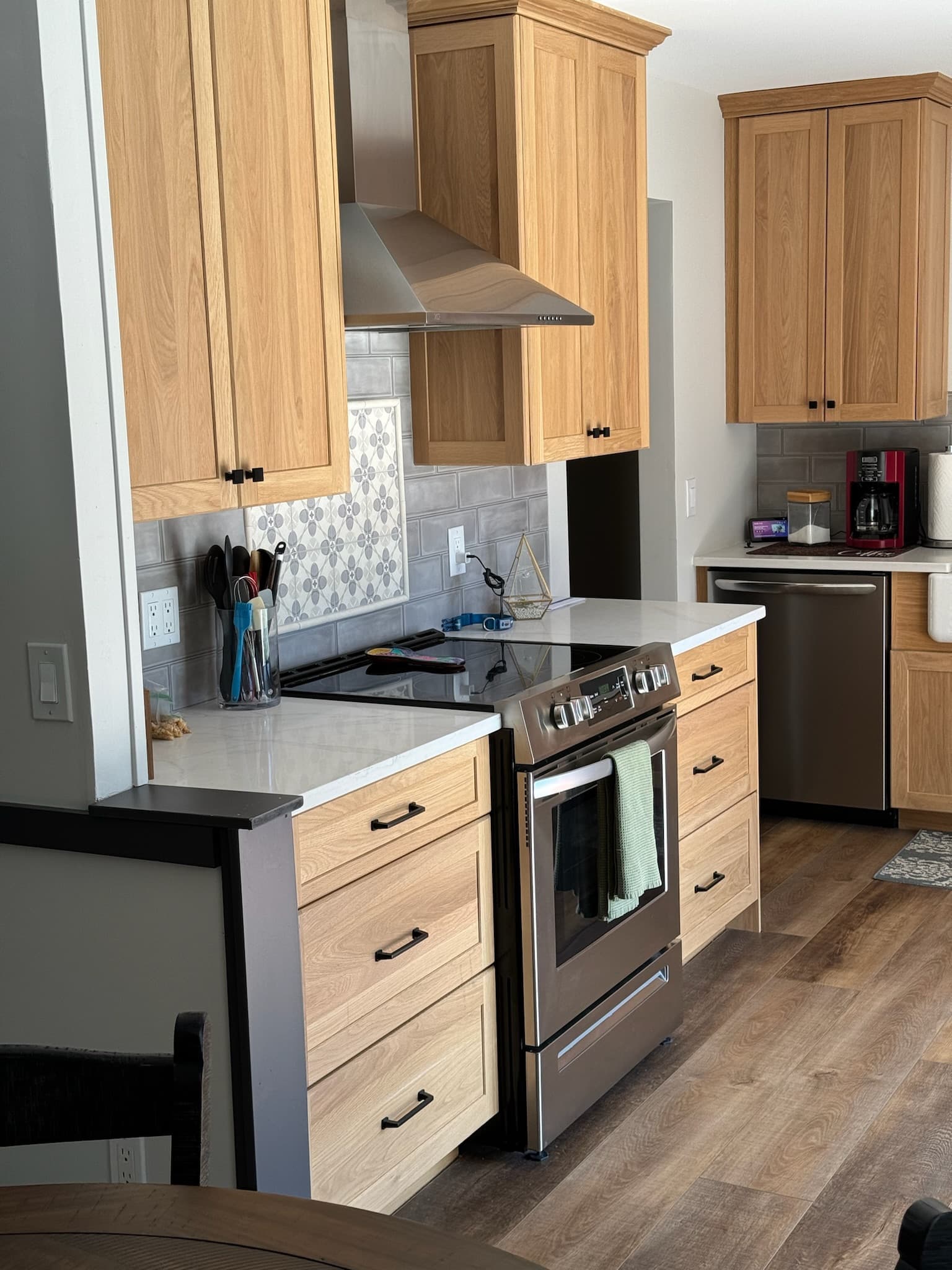 A bright transitional kitchen features light wood recessed panel cabinets, white quartz countertops, and a stainless steel range and hood