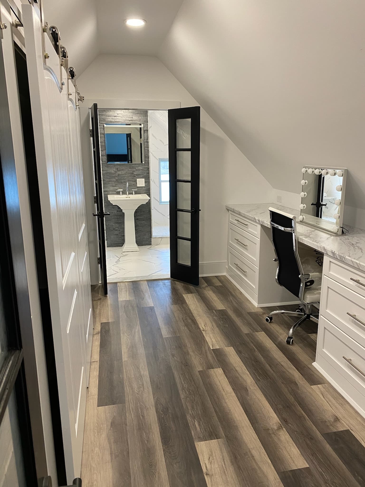 White vanity with marble countertop and a makeup mirror with lights in an attic bathroom with dark wood flooring