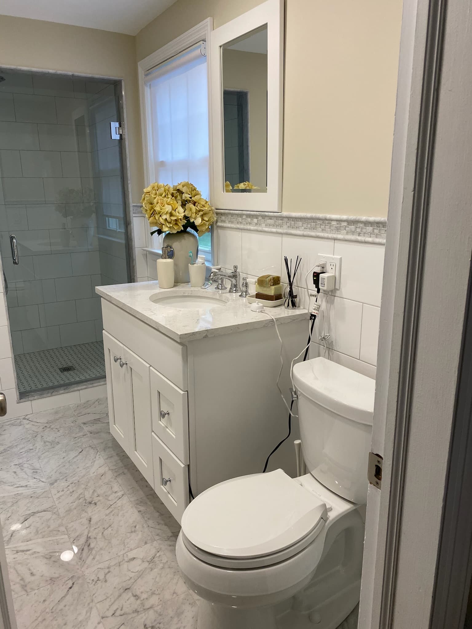 A white vanity with a quartz countertop, framed mirror, and brushed nickel hardware, next to a glass walk-in shower