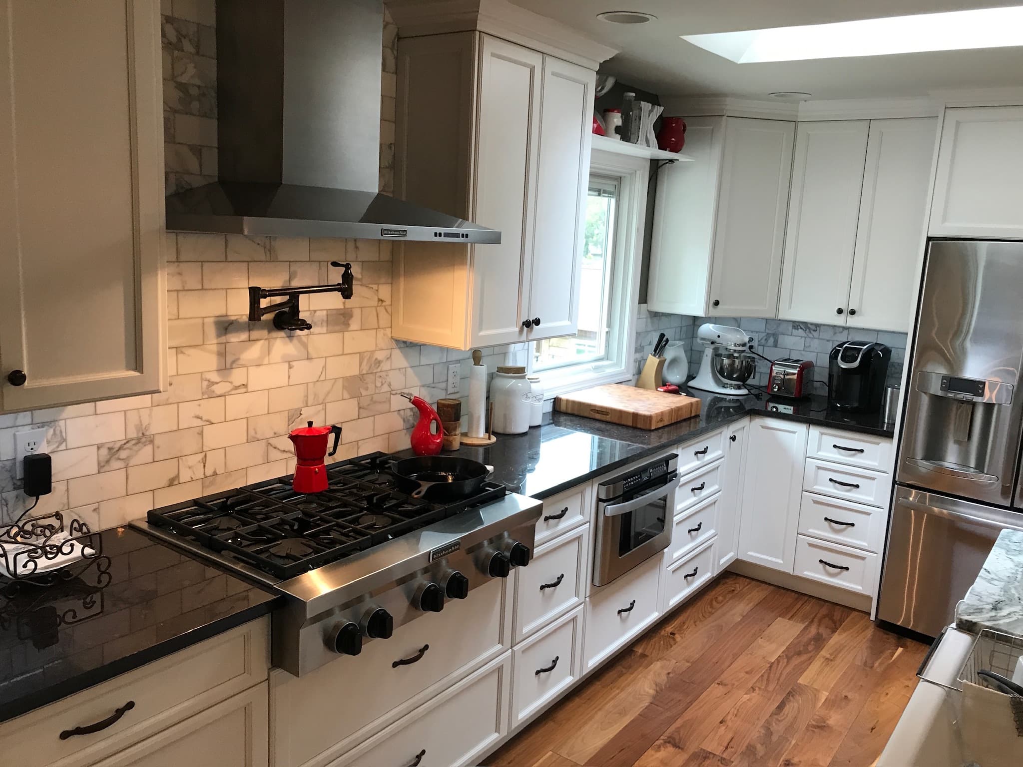 A transitional kitchen with two-tone cabinets, black granite countertops, stainless steel appliances, and a marble subway tile backsplash