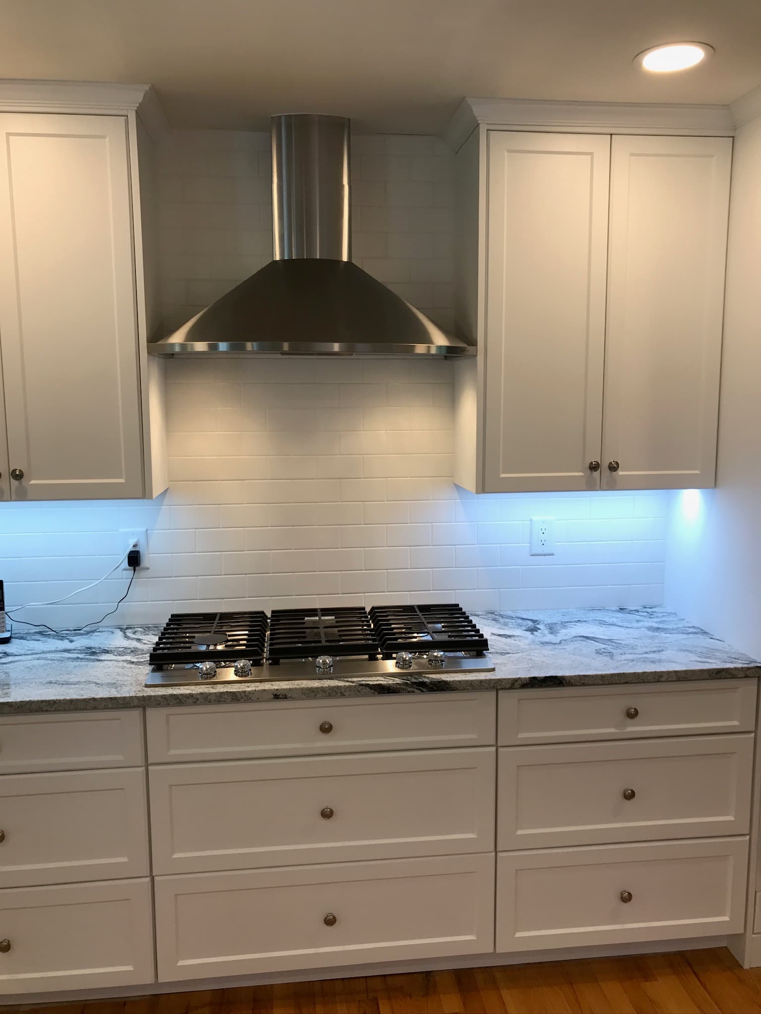 White shaker cabinets and granite countertops with a stainless steel range and hood in a transitional kitchen