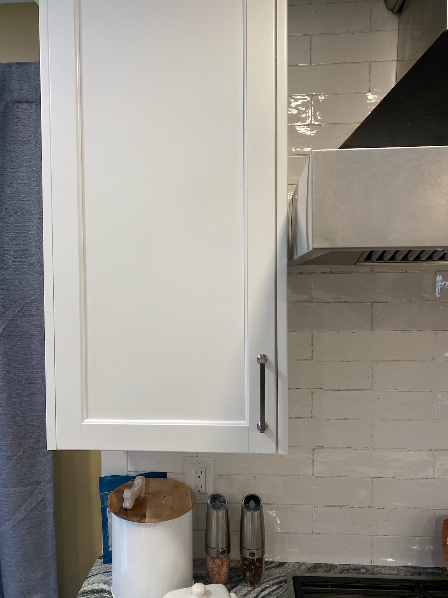 Close up of white shaker kitchen cabinets with brushed nickel hardware above a granite countertop and subway tile backsplash