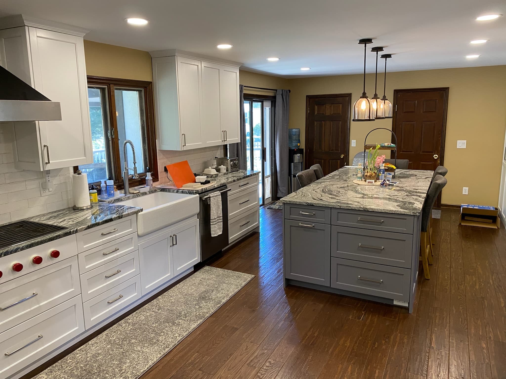 A bright transitional kitchen with white shaker perimeter cabinets, a gray island, granite countertops, and a farmhouse sink