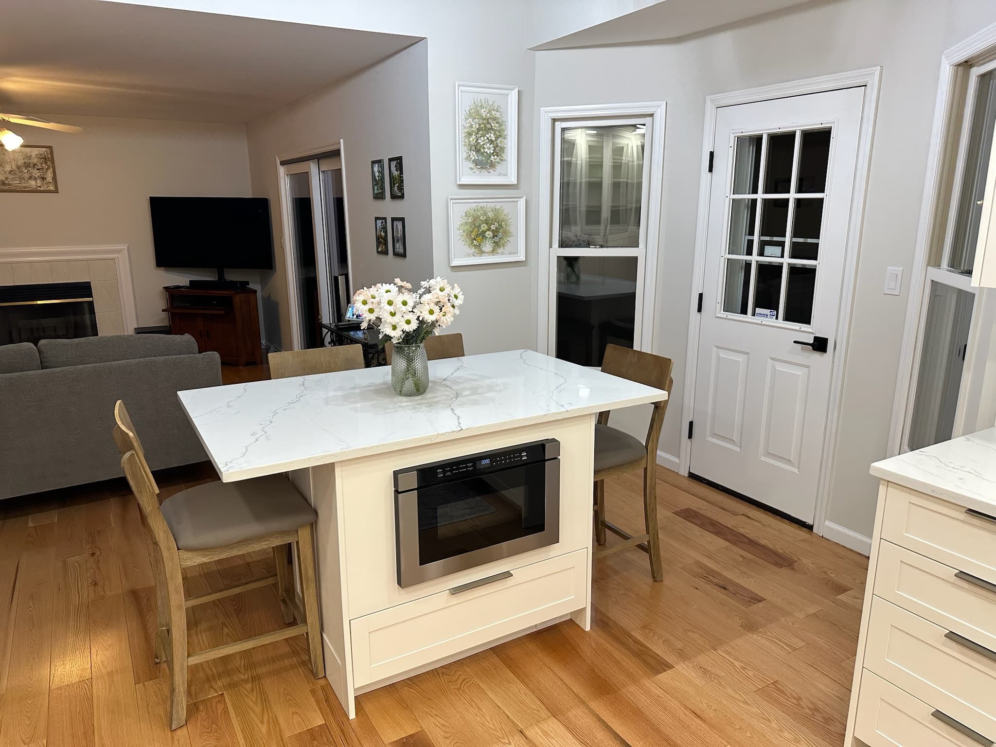 Kitchen features a beige shaker island with a white engineered quartz countertop, an under-counter microwave, and seating for two