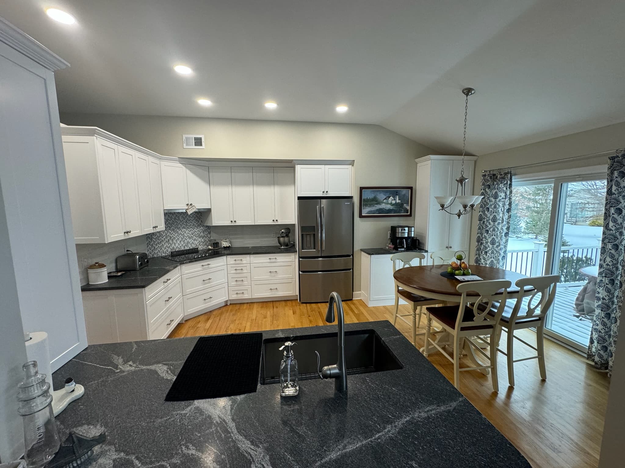 A bright transitional kitchen with white shaker cabinets, dark granite countertops, and a large island with a sink