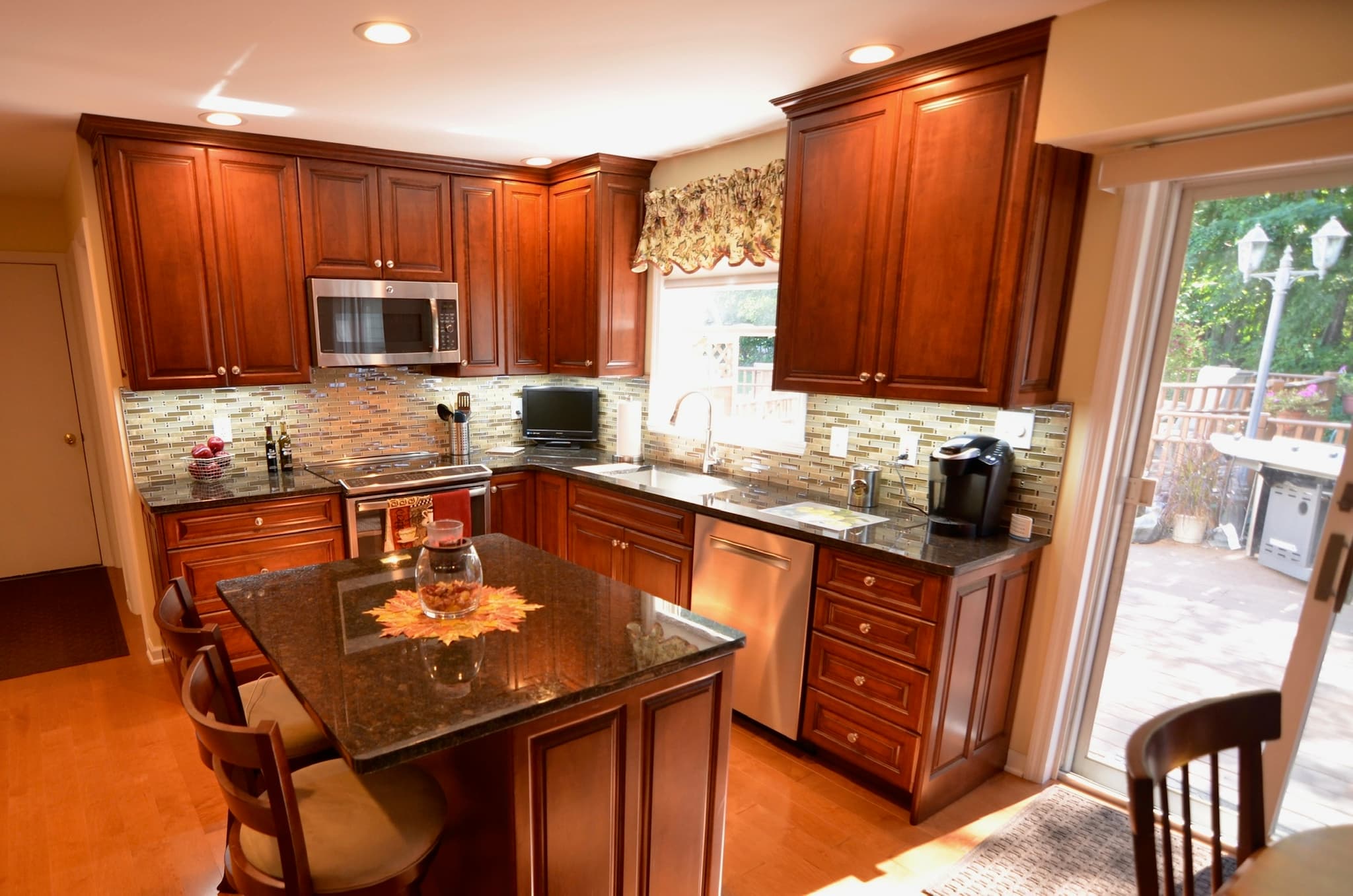 A transitional kitchen features medium wood raised panel cabinets, dark granite countertops, and an island with seating