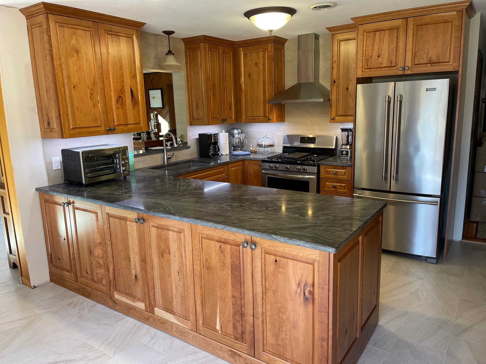 Wide shot of a transitional kitchen with medium wood raised panel cabinets, dark granite countertops, and stainless steel appliances