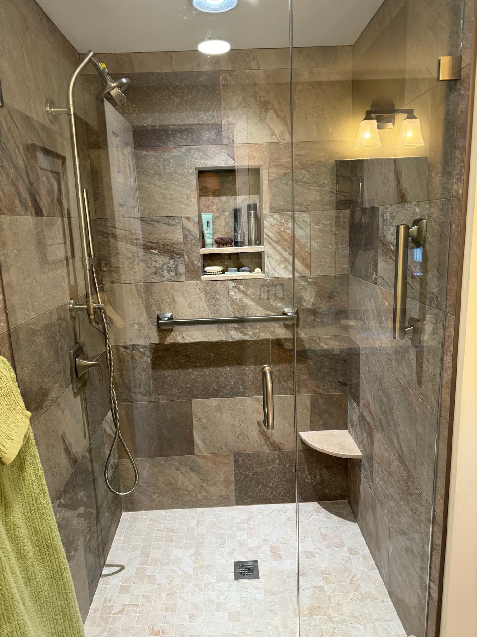 Shower with multi-toned brown and beige tiled walls and floor, a built-in niche, and brushed nickel fixtures