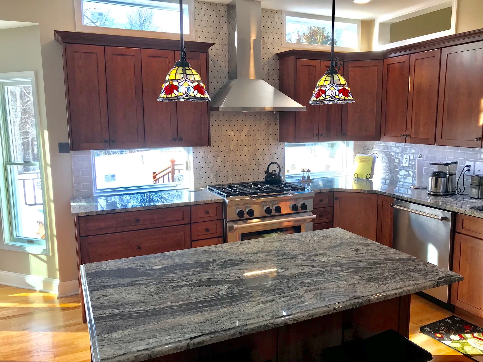 A transitional kitchen features medium wood cabinets, a granite island and countertops, stainless steel appliances, and decorative pendant lights