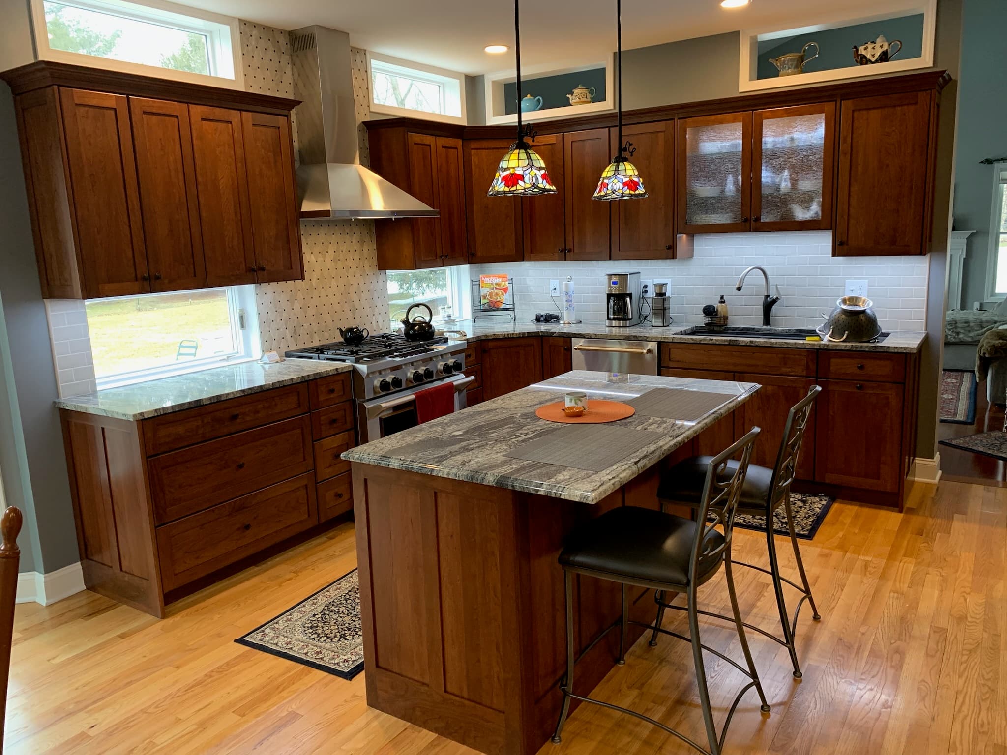A bright transitional kitchen with medium wood cabinetry, granite countertops, an island with a breakfast bar, and stainless steel appliances