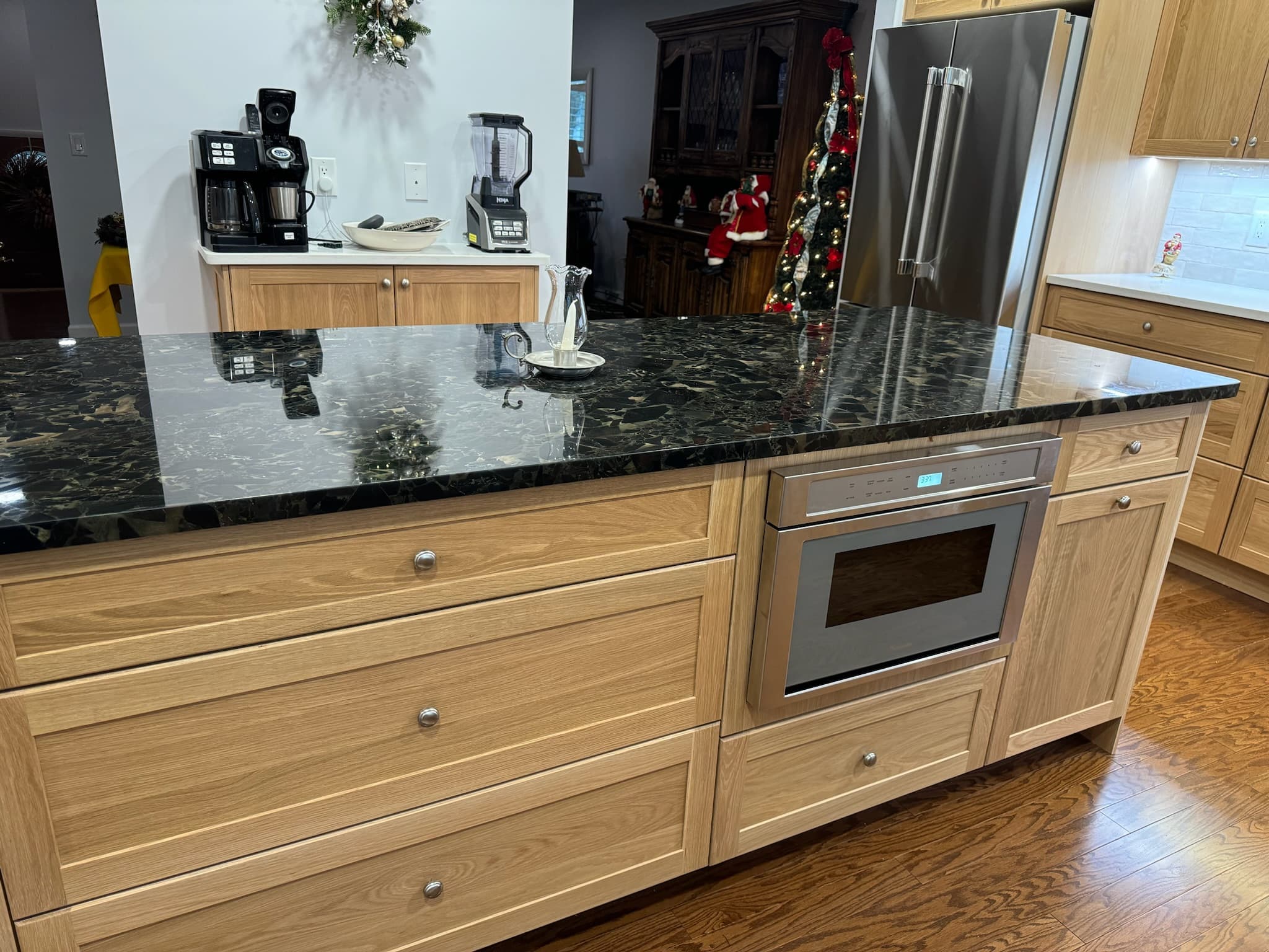 Kitchen island with light wood cabinets and a dark granite countertop, featuring an integrated microwave drawer and brushed nickel hardware