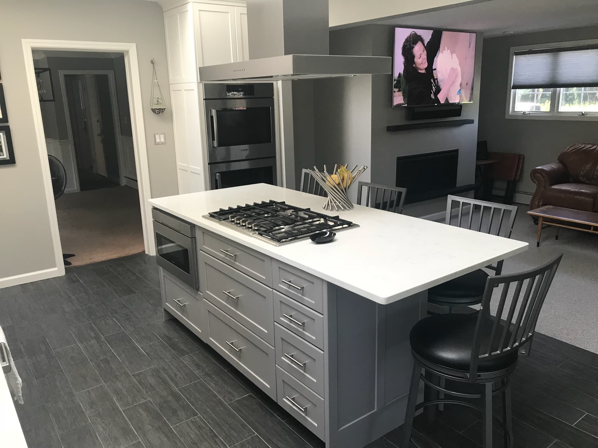 Wide view of a kitchen with a gray island, white perimeter cabinets, gas cooktop, double ovens, and white quartz countertops