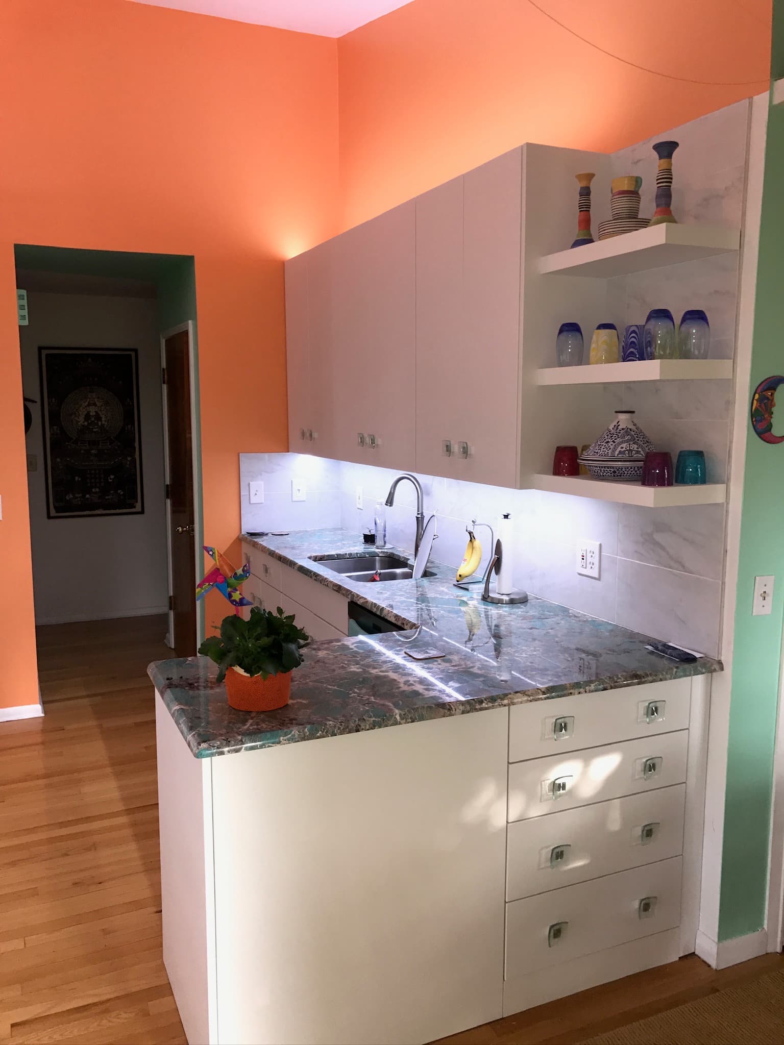 A contemporary kitchen features white slab cabinets with clear hardware, a green granite countertop, and open shelving