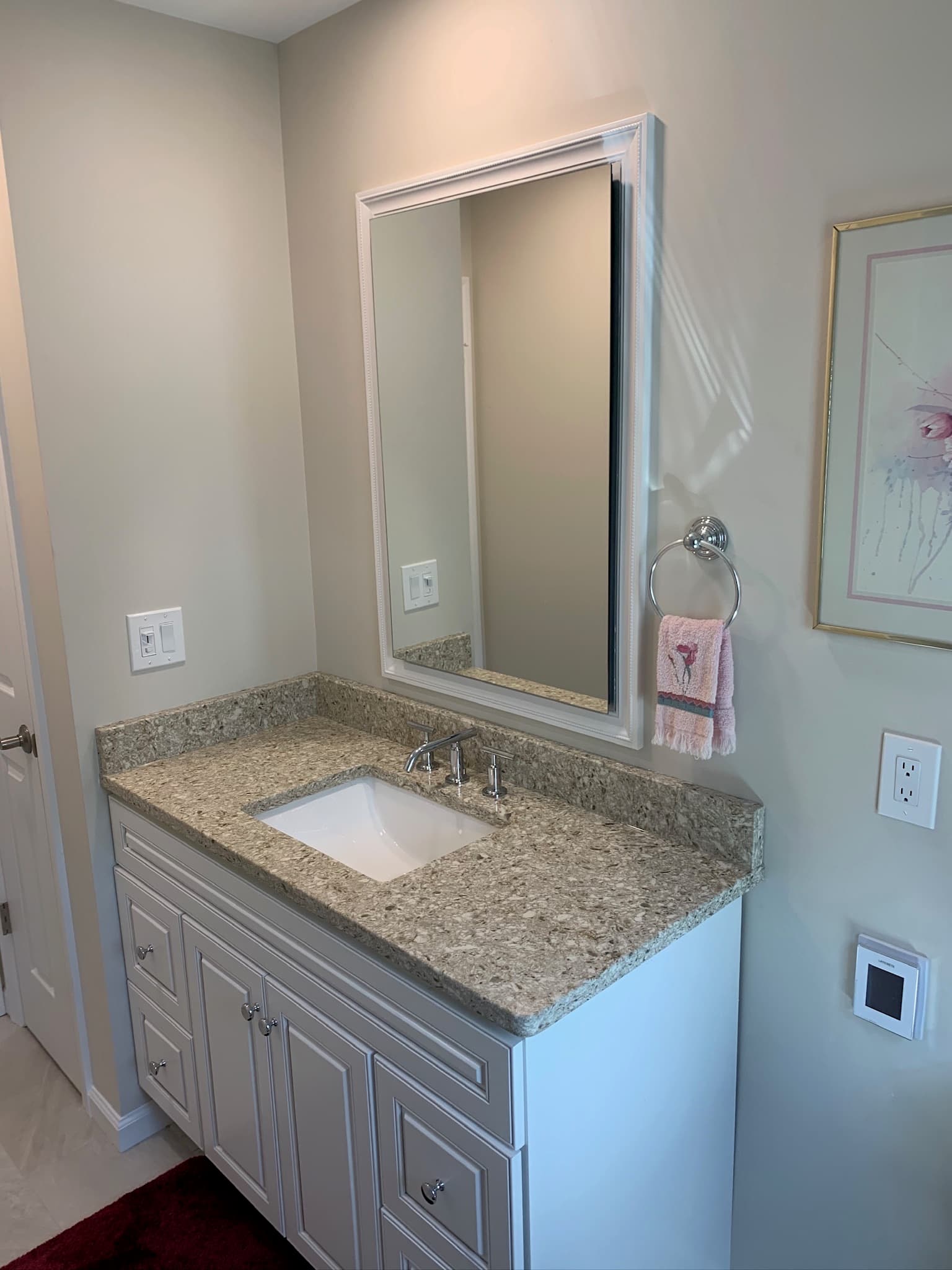 A white recessed panel single vanity with a granite countertop and chrome faucet in a transitional bathroom