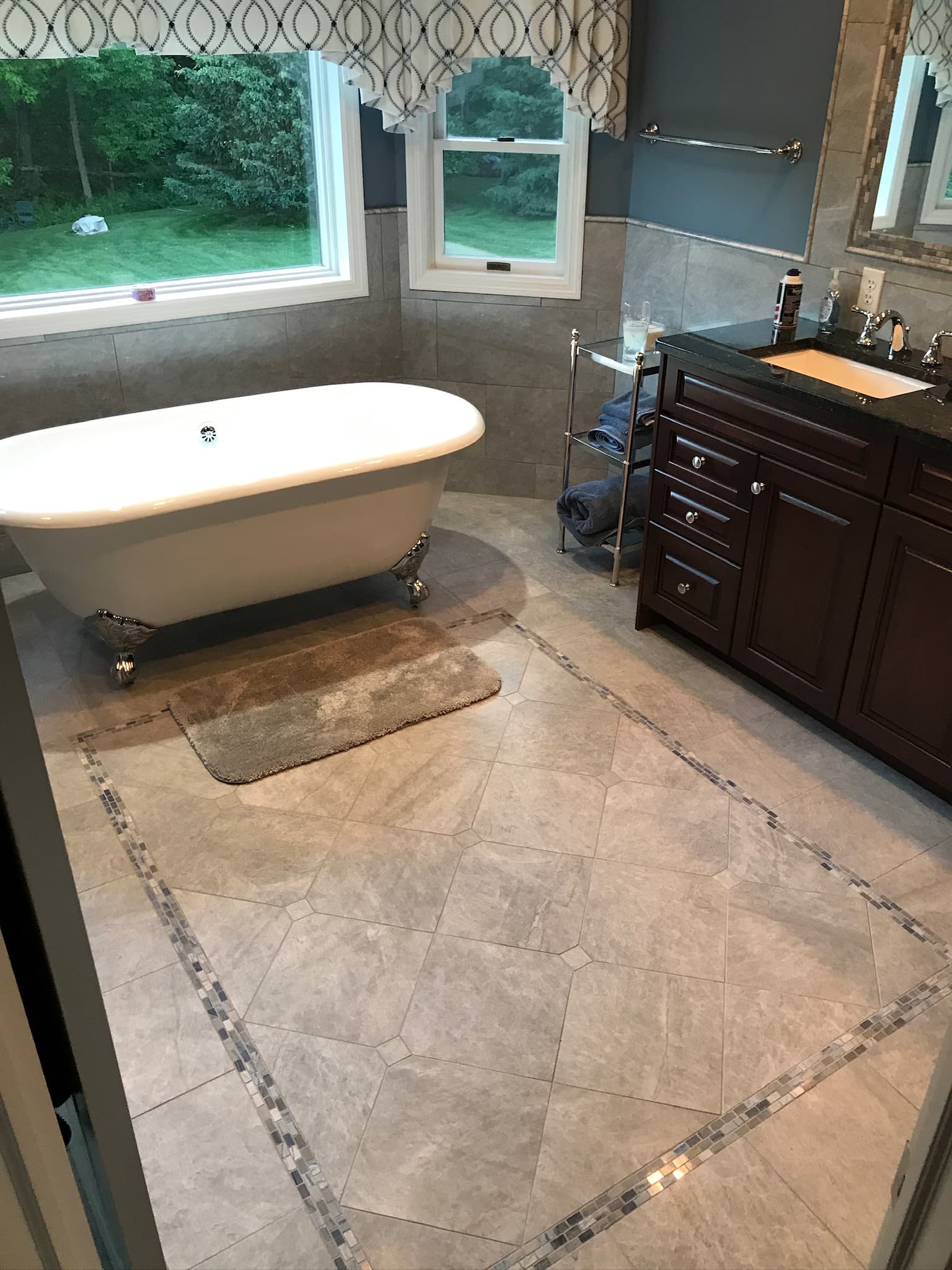 Transitional bathroom with dark wood vanity, granite countertop, and a freestanding clawfoot tub under two windows