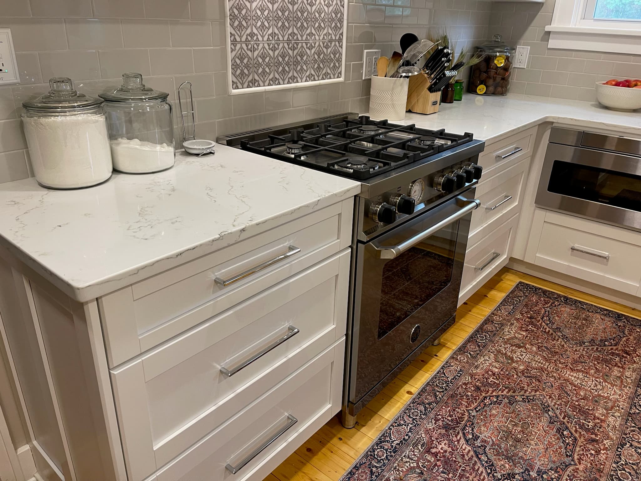 A bright kitchen features white shaker cabinets, stainless steel range and microwave, and white quartz countertops
