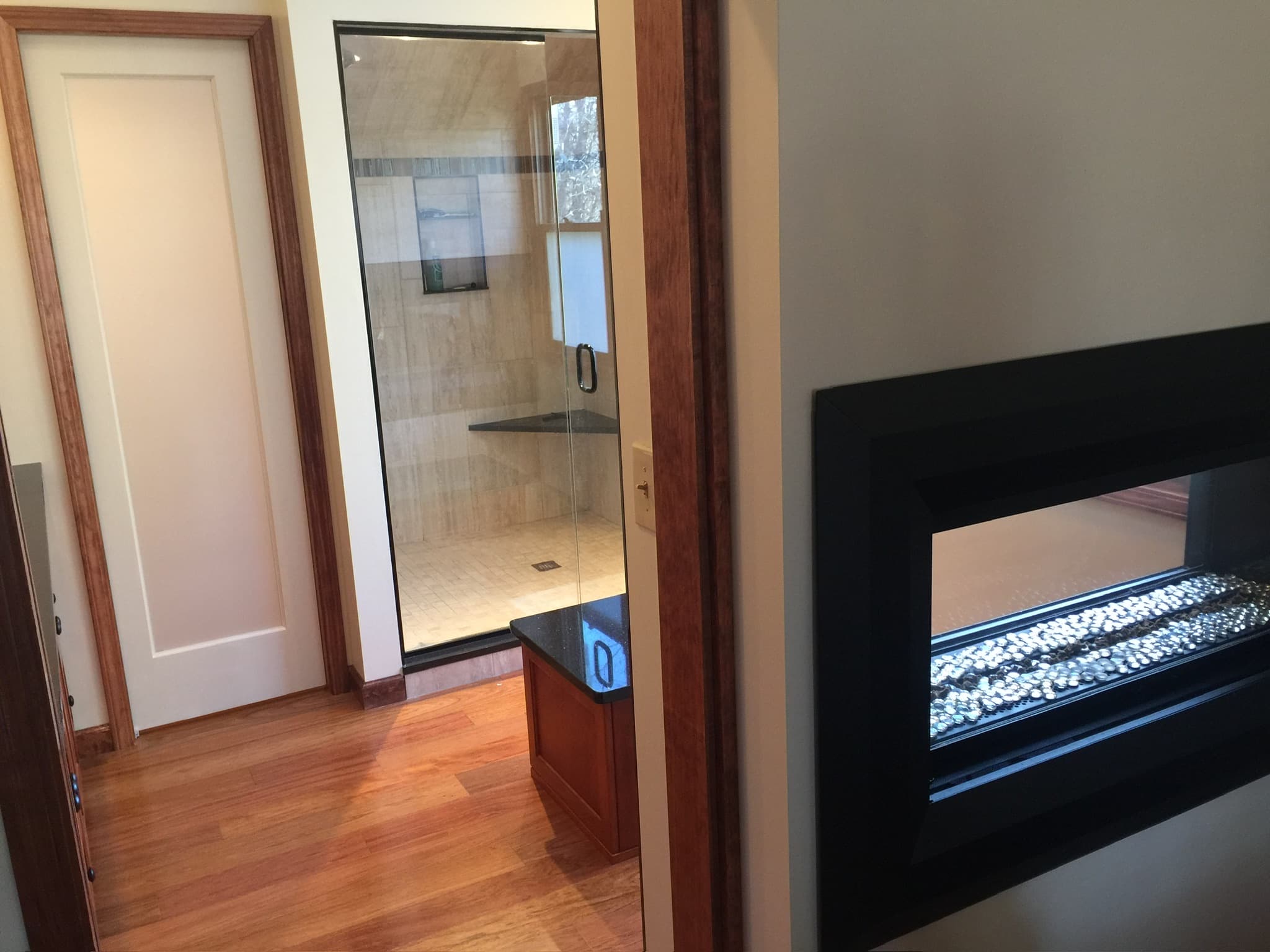 View into a bathroom with a walk-in shower featuring tiled walls and a bench, next to a small medium-wood cabinet with a dark countertop