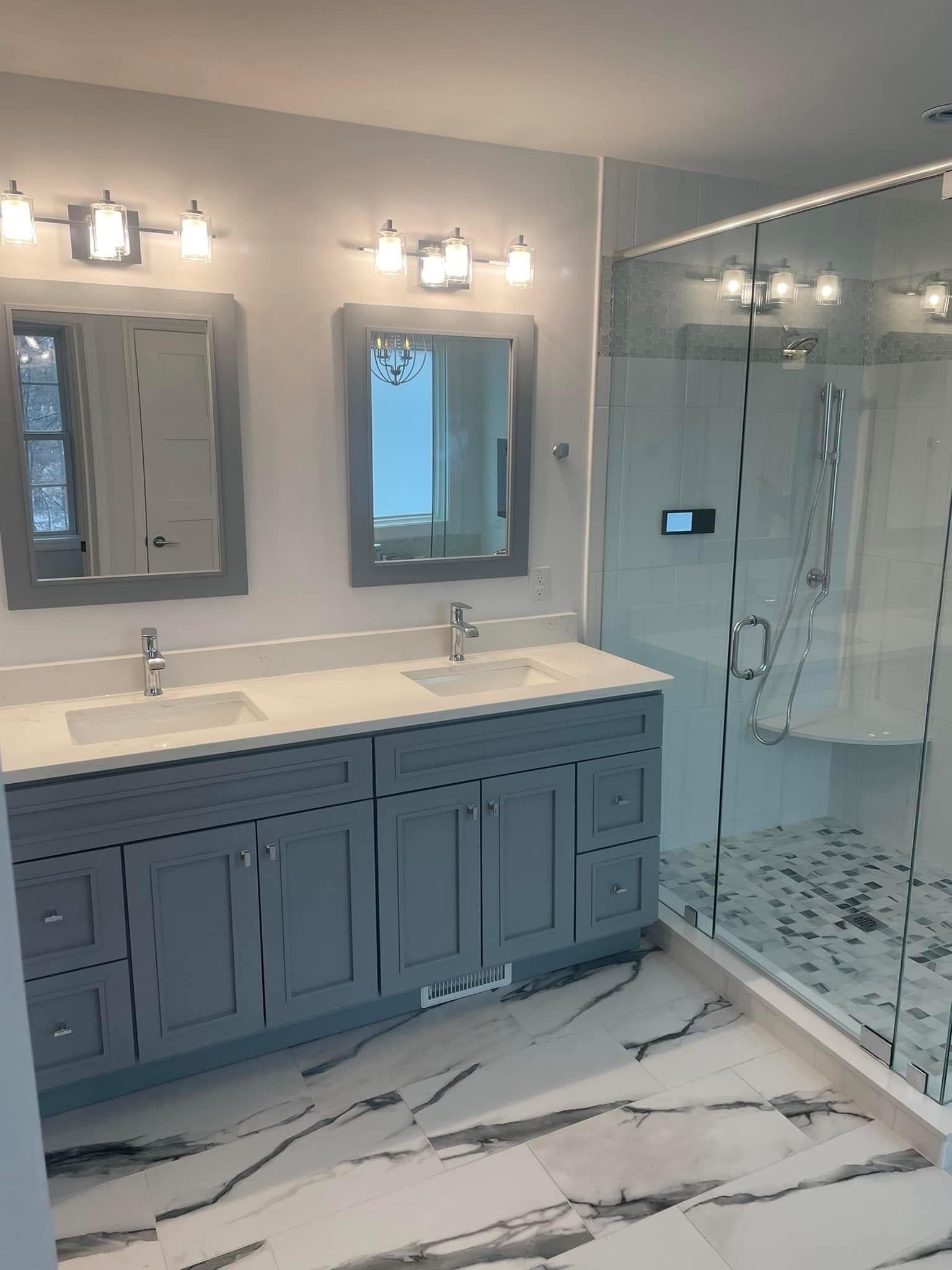 A bright transitional bathroom features a gray double vanity with white quartz countertop, chrome fixtures, and a glass-enclosed walk-in shower