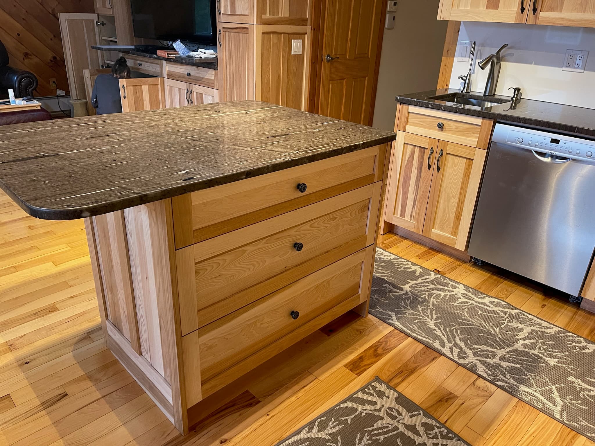 Light wood kitchen island with dark granite countertop and a stainless steel dishwasher visible to the right