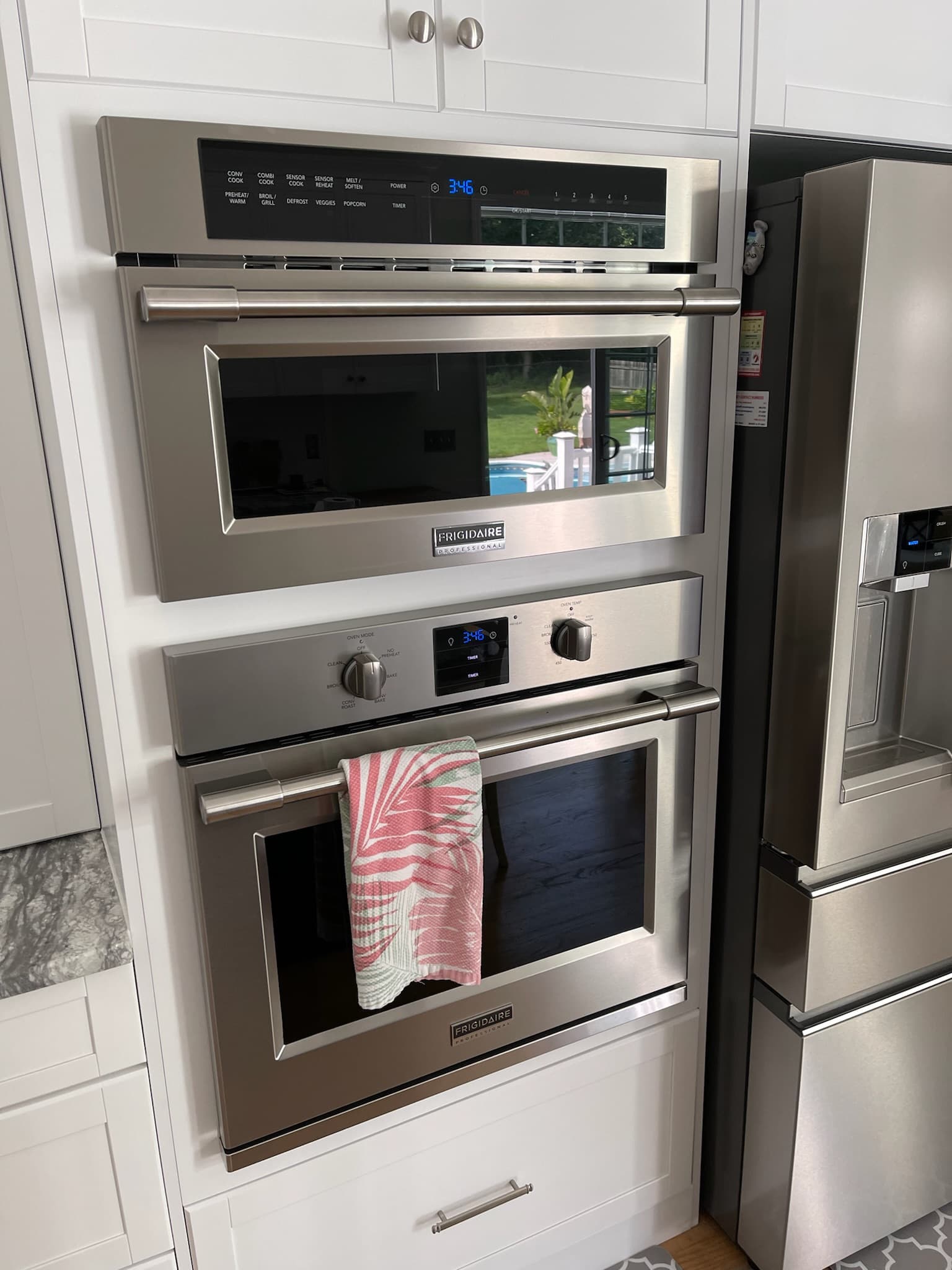 Close-up of stainless steel built-in oven, microwave, and refrigerator in a white transitional kitchen with shaker cabinets