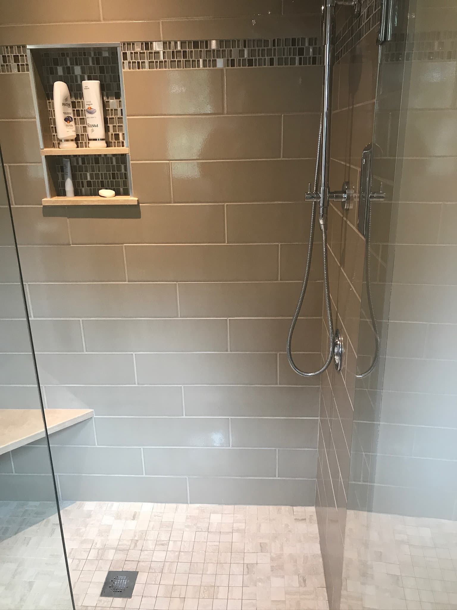 A walk-in shower with light brown subway tiles, a mosaic tile accent, and a built-in niche with wood shelves