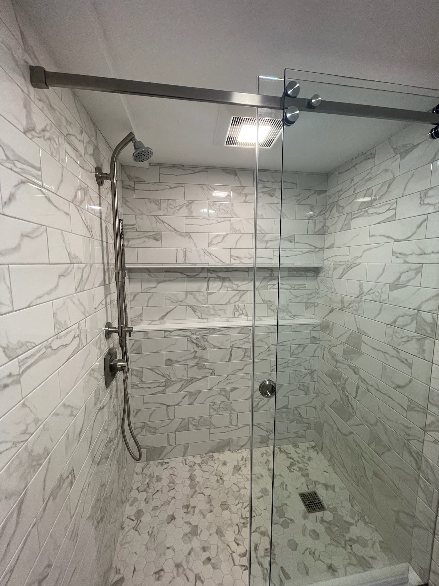 Modern walk-in shower with large format white subway tiles with gray veining and hexagonal floor tiles
