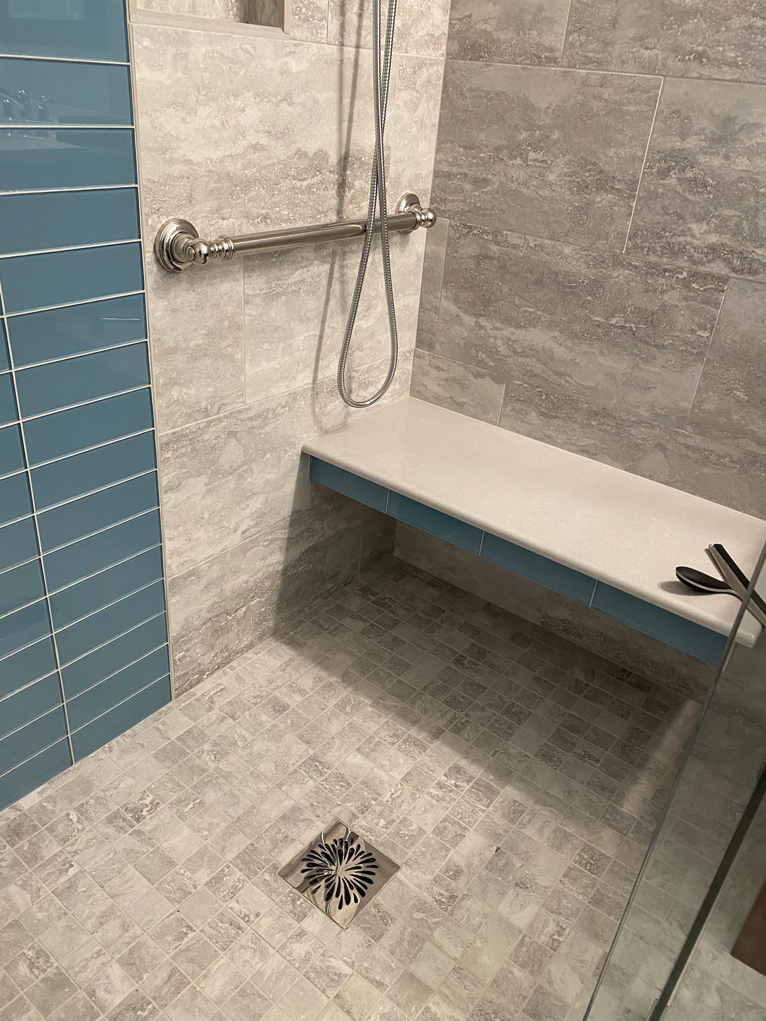 Walk-in shower with light gray patterned tile walls, a blue subway tile accent, a built-in bench, and a brushed nickel grab bar