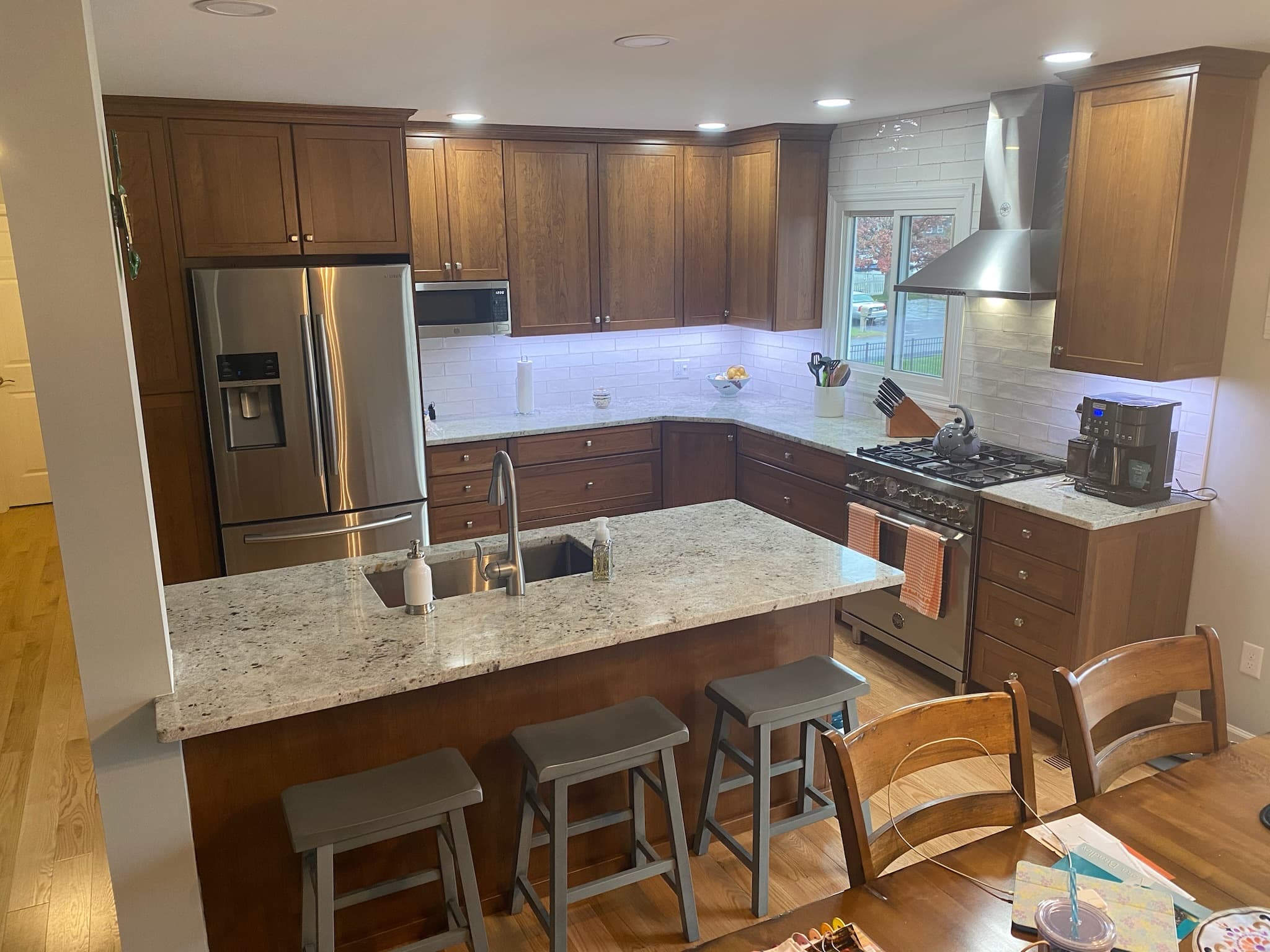 Wide view of a transitional kitchen with medium wood cabinets, light granite countertops, a kitchen island with seating, and stainless steel appliances