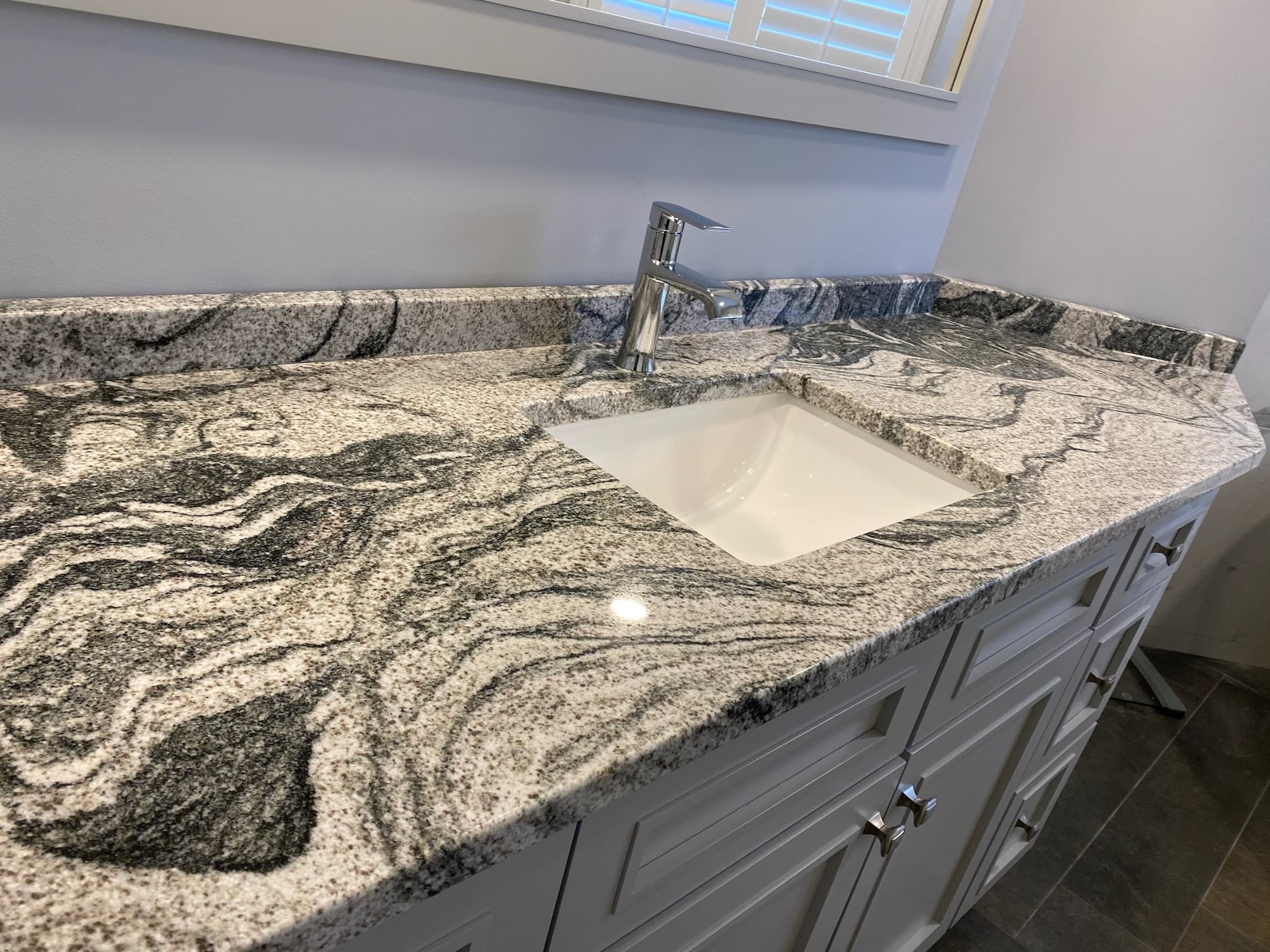 Light gray shaker vanity with a dramatic granite countertop and undermount sink in a transitional Saratoga Springs bathroom