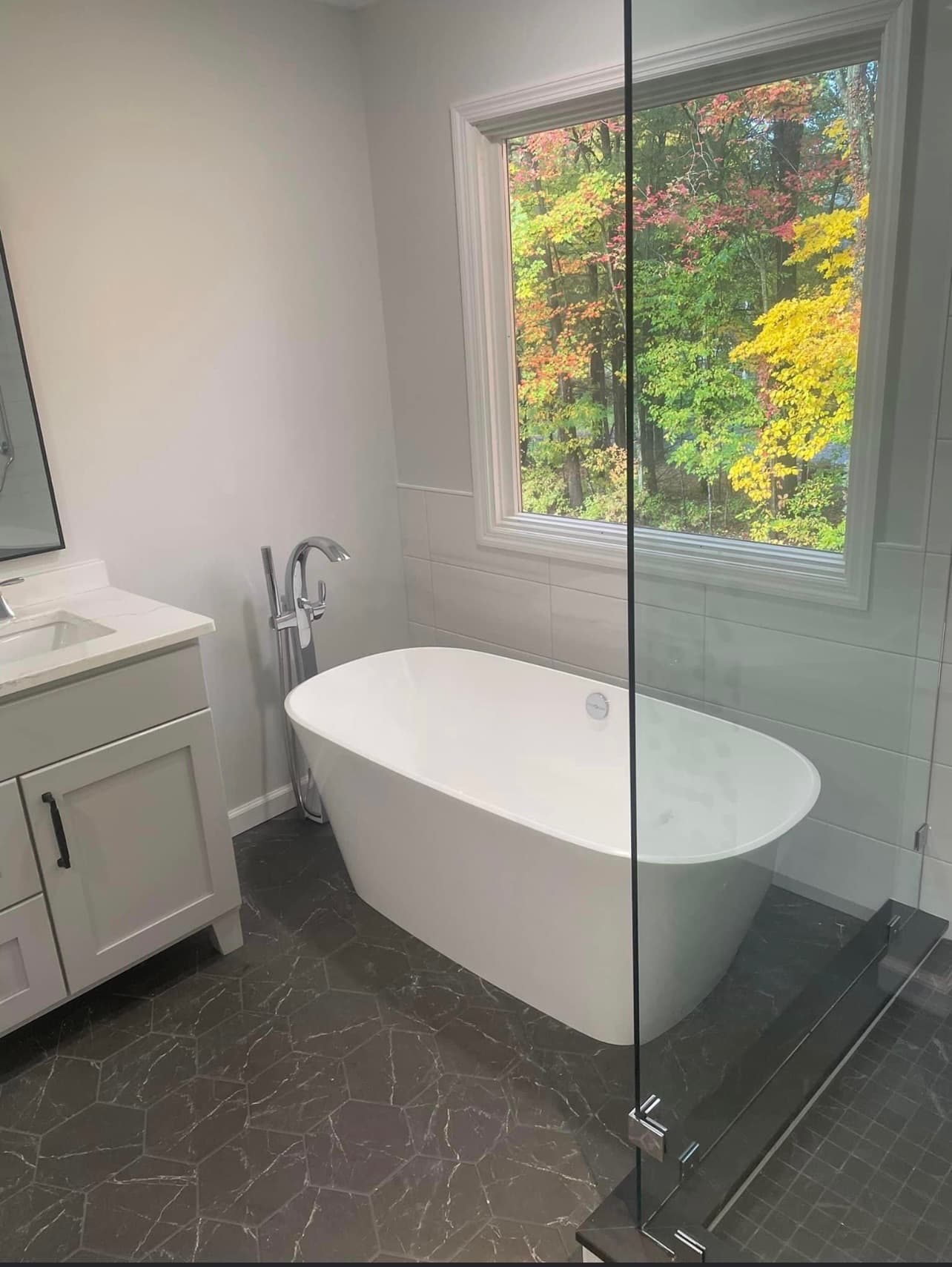 Modern bathroom with a freestanding tub, gray shaker vanity, white quartz countertop, and black patterned floor tiles