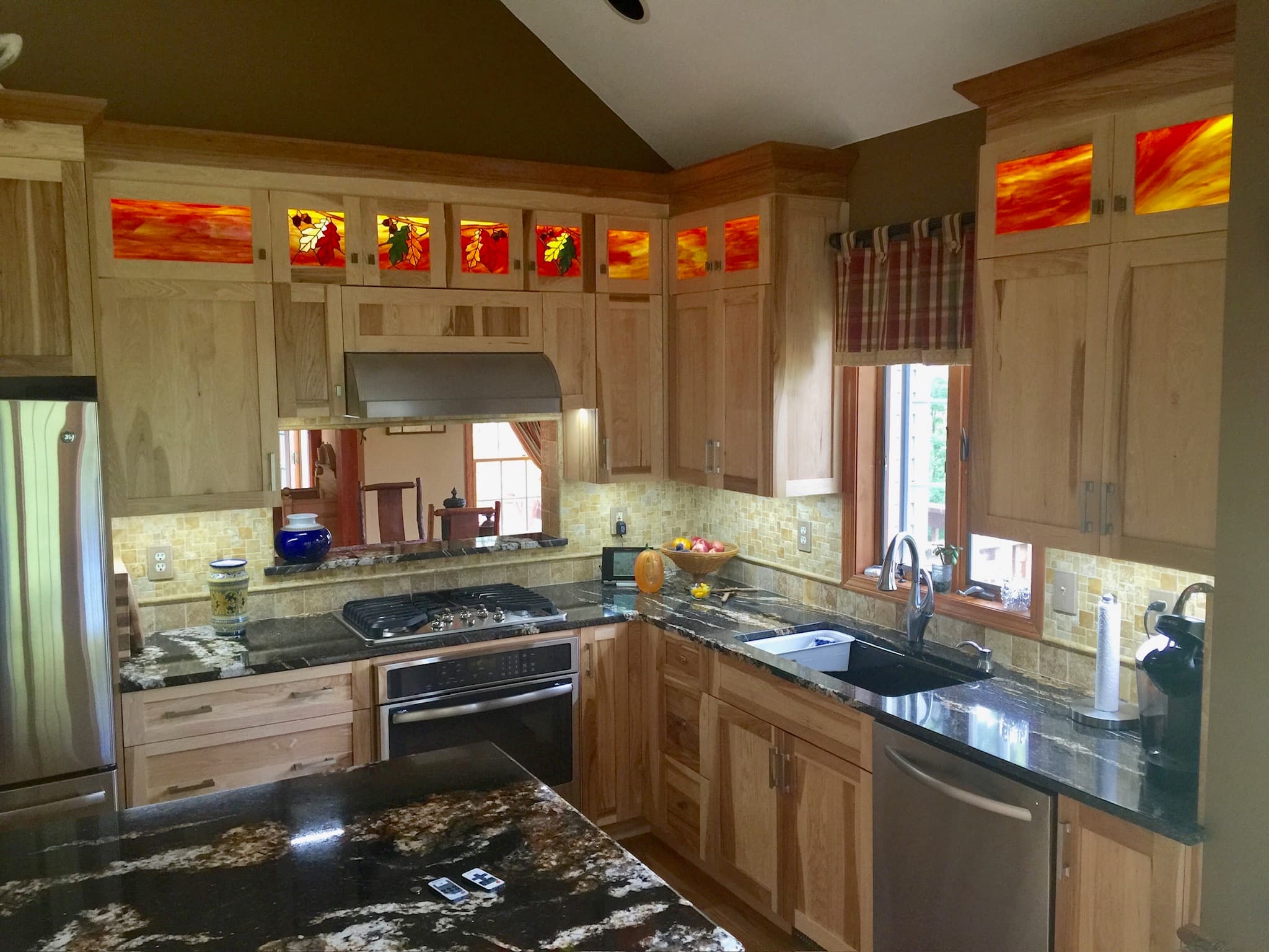 Traditional kitchen with light wood cabinets, black granite countertops, mosaic tile backsplash, and decorative stained glass panels