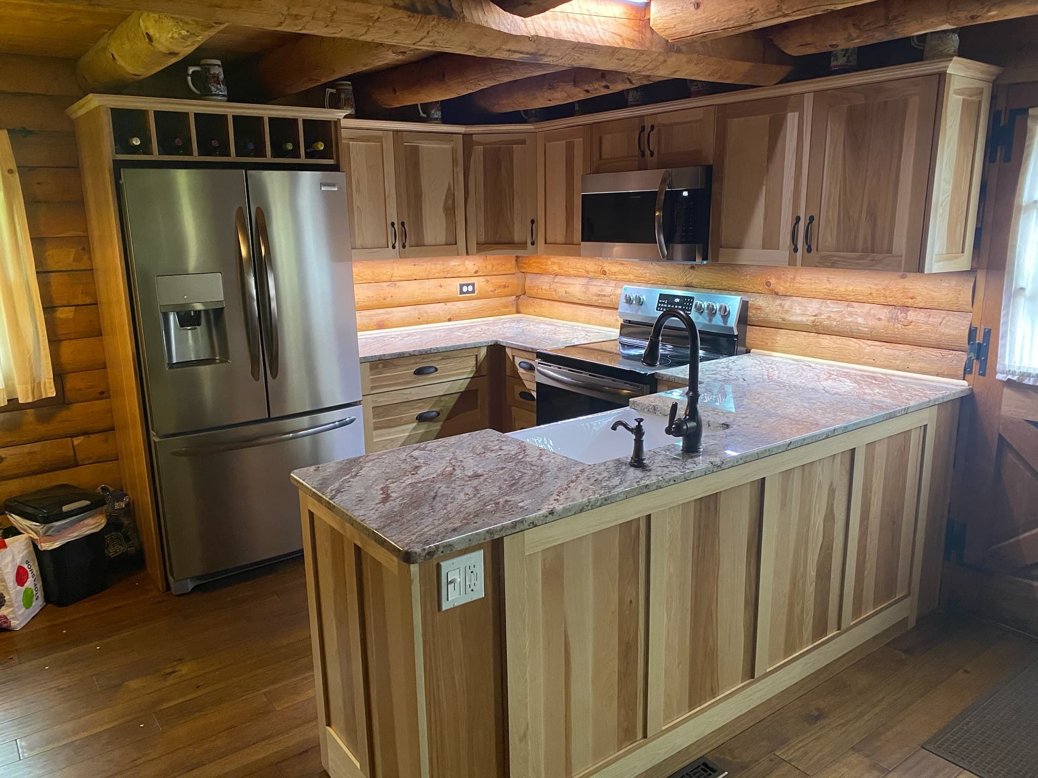 Rustic kitchen with light wood recessed panel cabinets, granite countertops, an island with a sink, and integrated wine storage