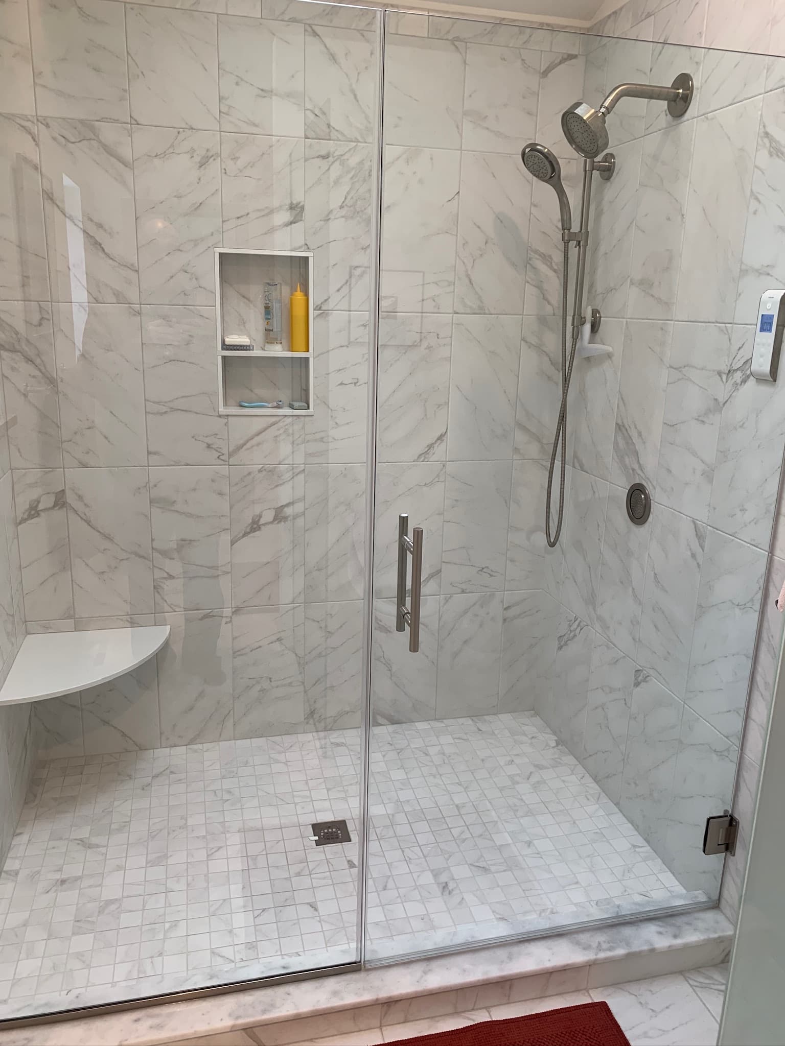 A bright transitional bathroom features a walk-in shower with white and gray marble-look tile, a shower niche, and brushed nickel fixtures