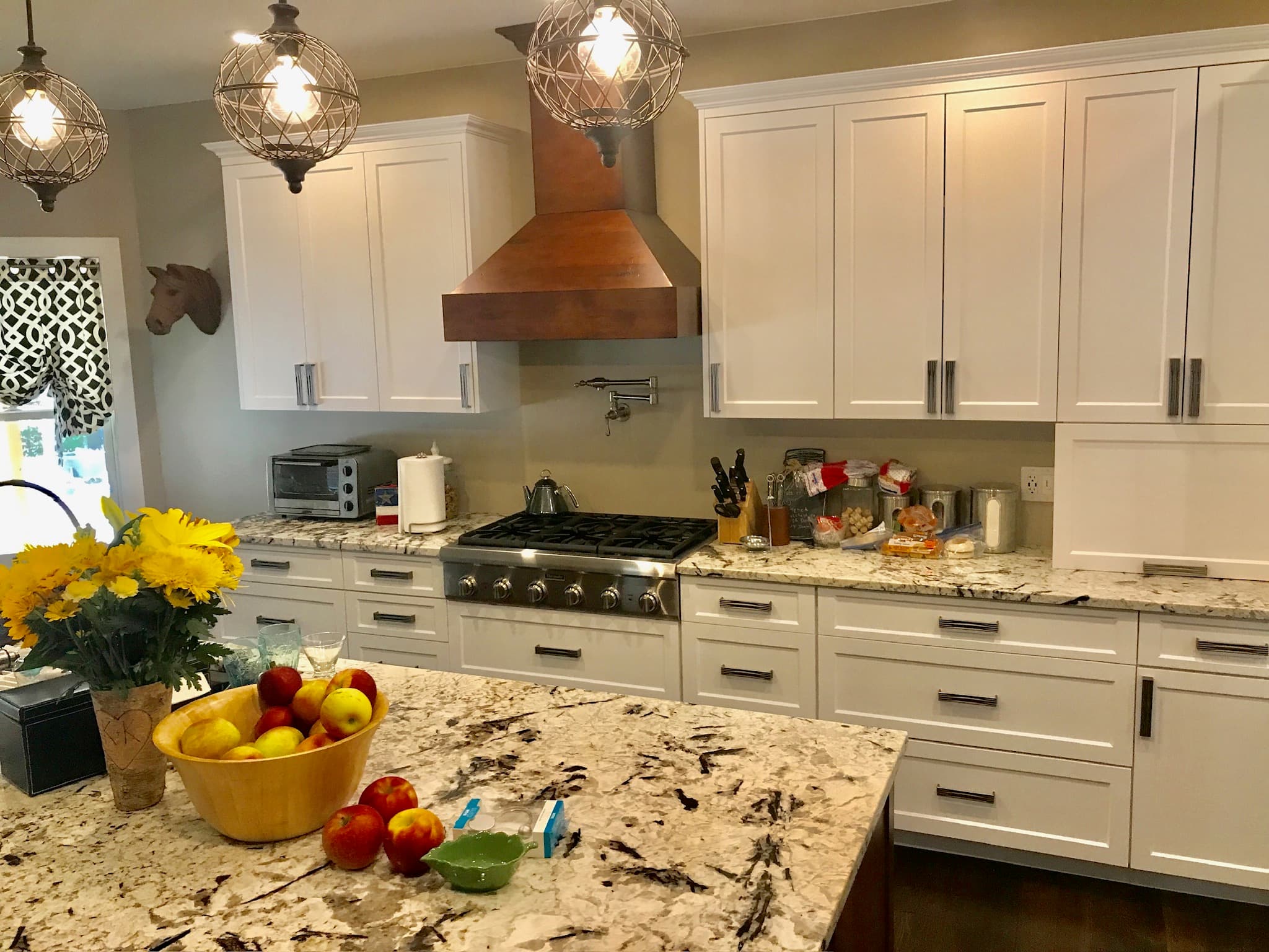 A transitional kitchen features white shaker cabinets, a striking dark wood range hood, granite countertops, and a large island