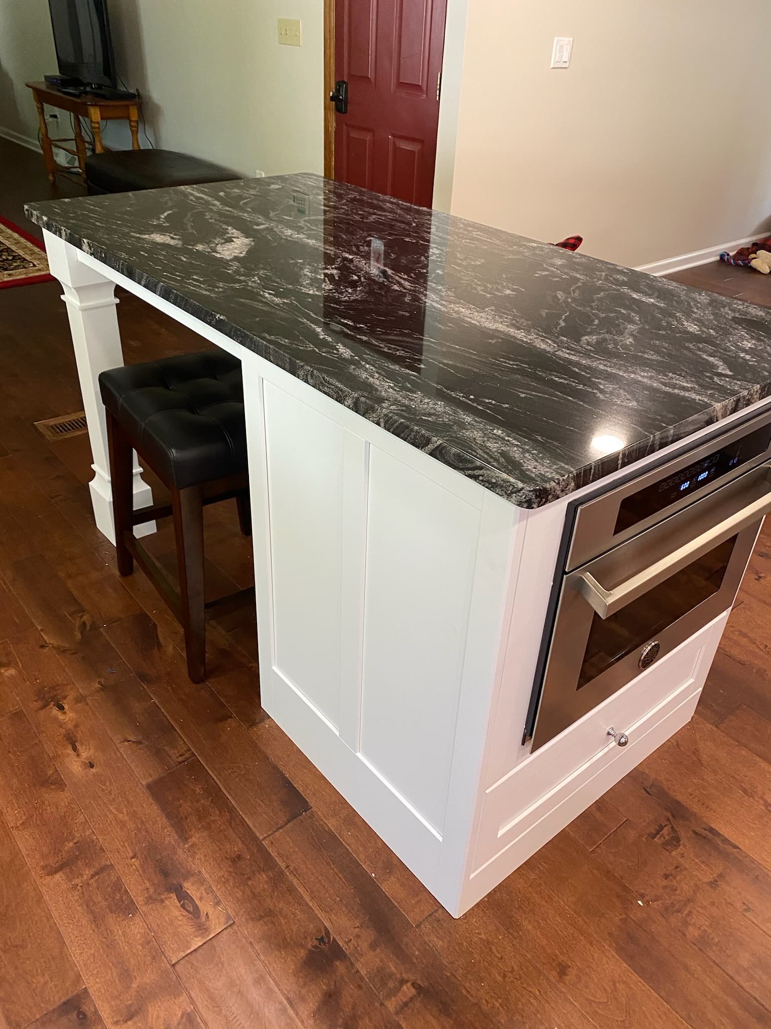 White kitchen island with a black granite countertop and under-counter microwave oven, with a leather bar stool