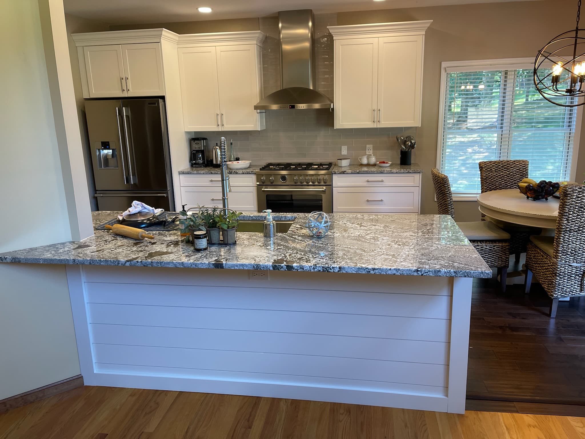 A transitional kitchen with white shaker cabinets, granite countertops, and a large kitchen island with shiplap-style paneling