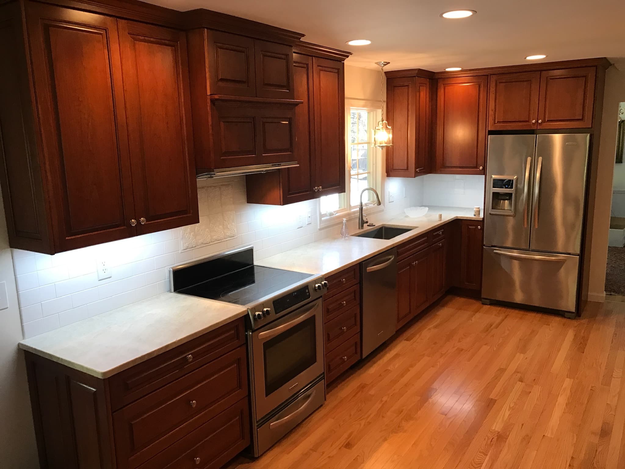 Wide shot of a transitional kitchen with dark wood raised panel cabinets, light quartz countertops, and white subway tile backsplash