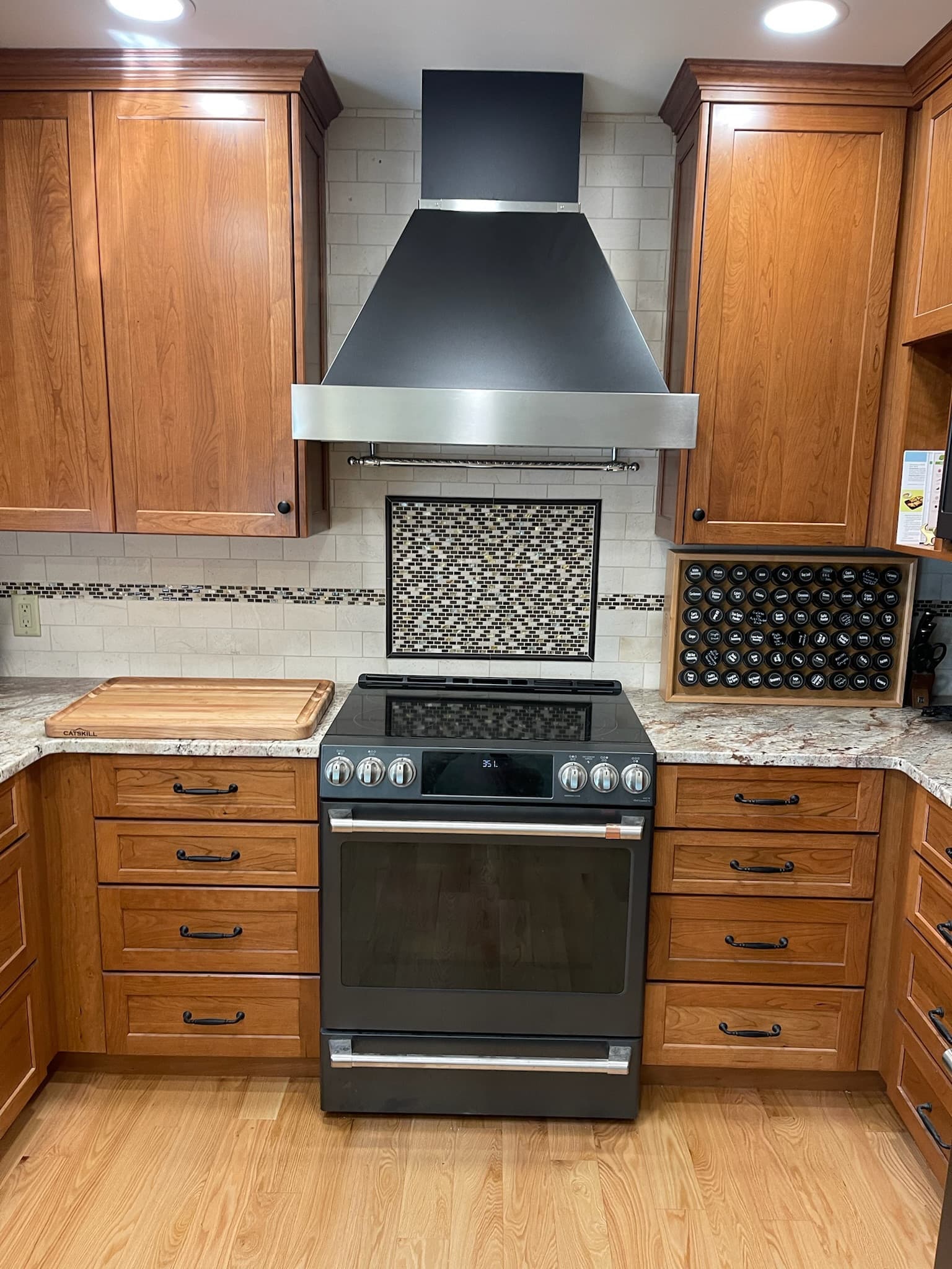 Kitchen with medium wood raised panel cabinets, granite countertops, and a black and stainless steel range hood above a black electric range