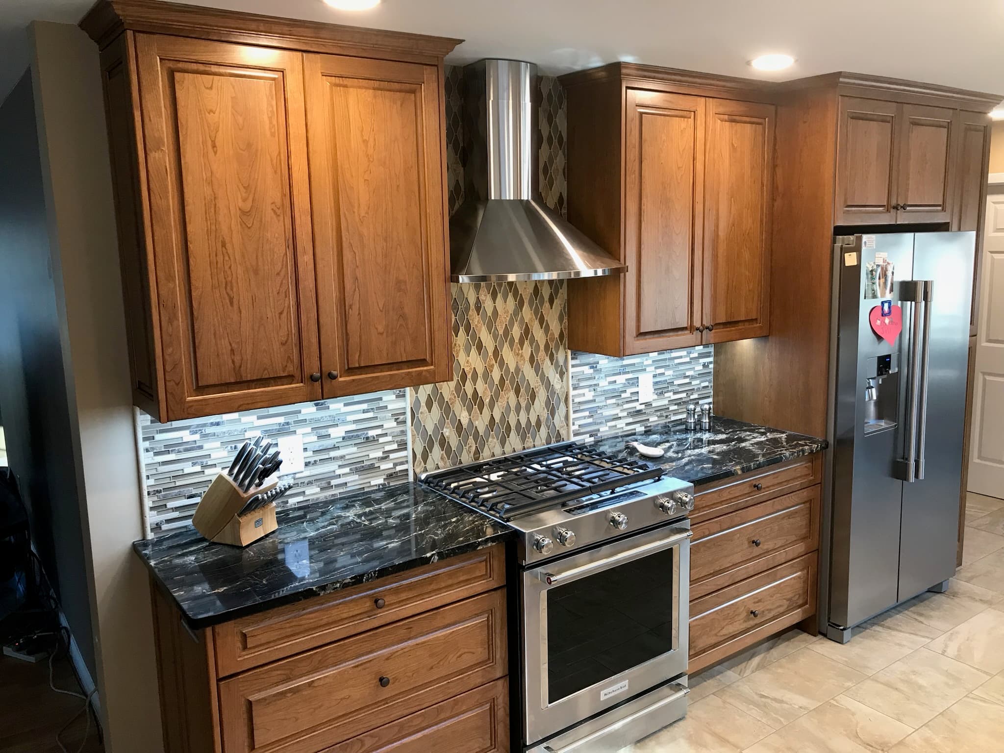Kitchen with medium wood raised-panel cabinets, dark granite countertops, stainless steel appliances, and mosaic tile backsplash