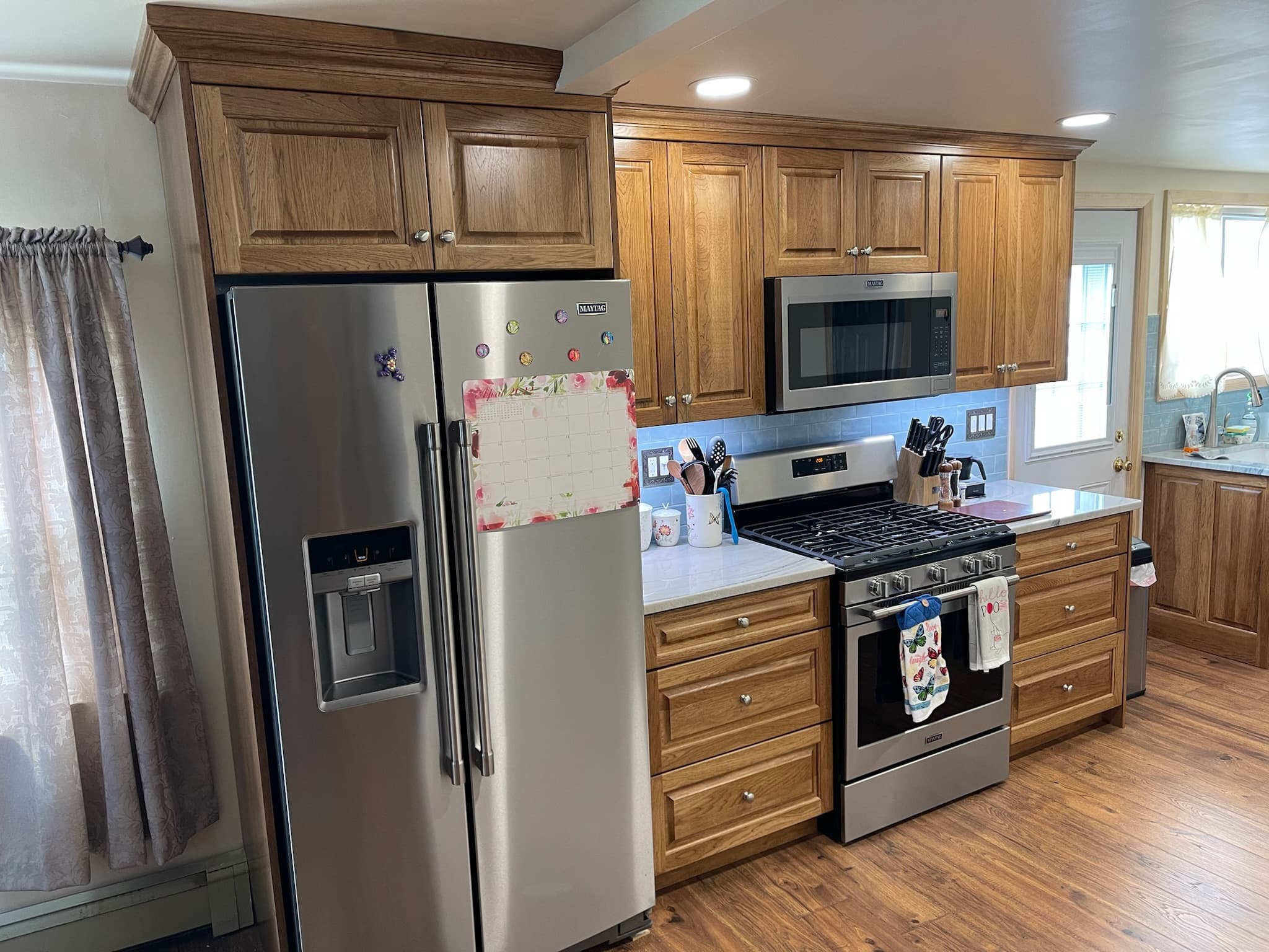 A traditional kitchen features medium wood raised panel cabinets, stainless steel appliances, and light blue subway tile backsplash